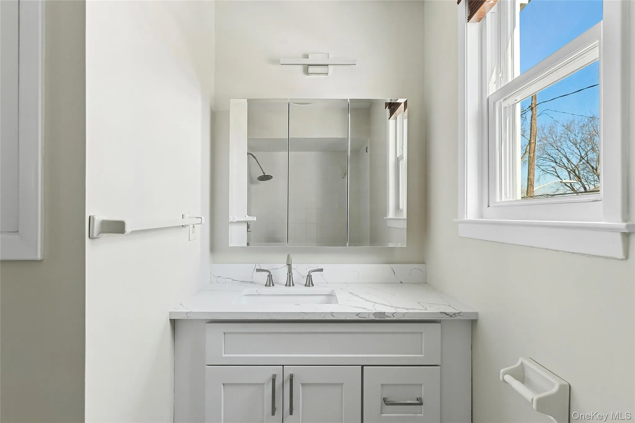 Bathroom vanity with white shaker-style cabinetry, a white countertop with gray veining, and a polished chrome faucet Bathroom vanity with white shaker-style cabinetry, a white countertop with gray veining, and a polished chrome faucet