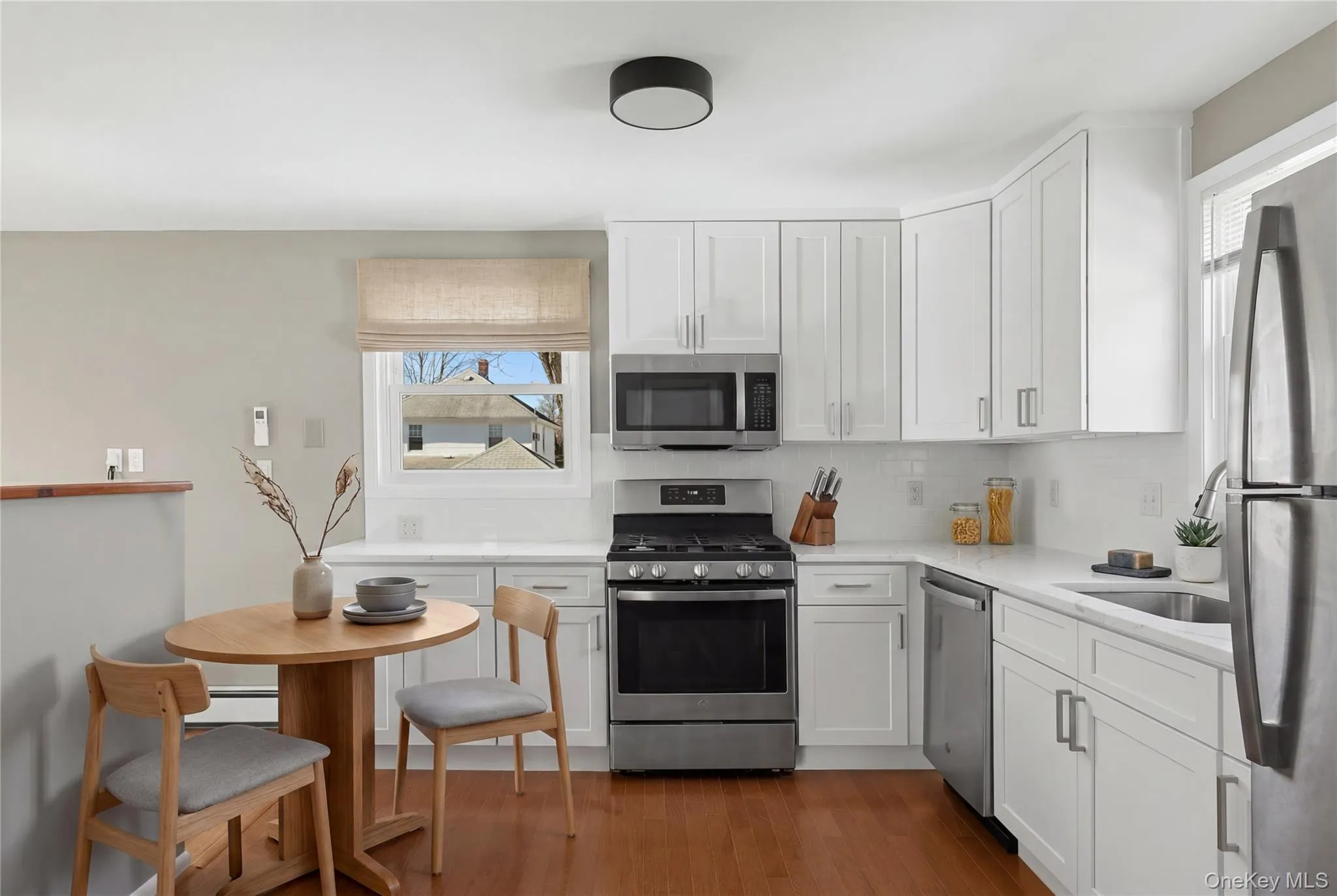 Modern kitchen featuring white shaker cabinetry, stainless steel appliances, white countertops, a white subway tile backsplash, and wood-finish flooring Modern kitchen featuring white shaker cabinetry, stainless steel appliances, white countertops, a white subway tile backsplash, and wood-finish flooring