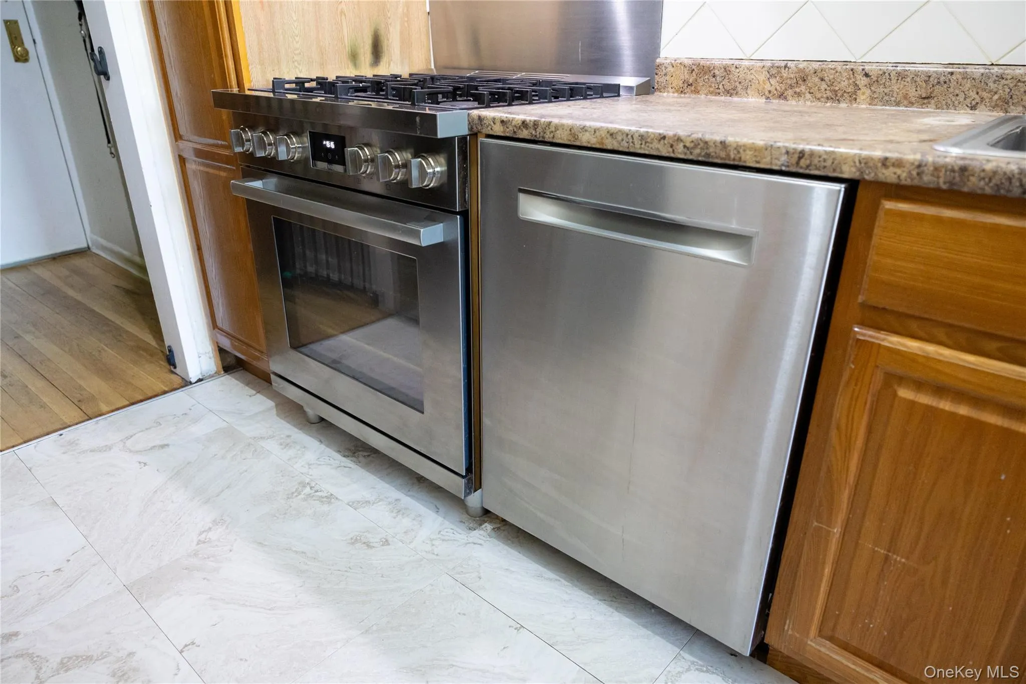 Stainless steel range and dishwasher complement wood cabinetry and a stone-finish countertop Stainless steel range and dishwasher complement wood cabinetry and a stone-finish countertop