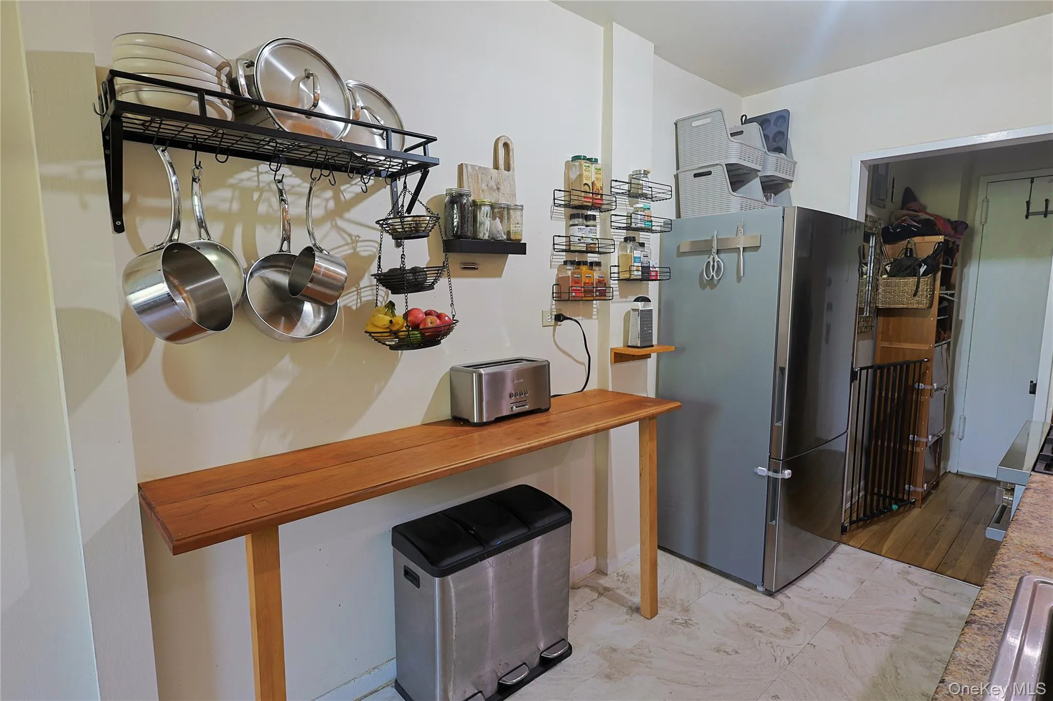 Compact kitchen space featuring a stainless steel refrigerator, a wall-mounted pot rack, and a wood-table top Compact kitchen space featuring a stainless steel refrigerator, a wall-mounted pot rack, and a wood-table top