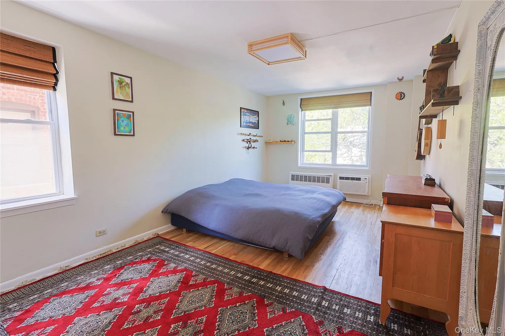 Bedroom featuring wood-finish flooring, two large windows with horizontal blinds, and a ceiling-mounted light fixture Bedroom featuring wood-finish flooring, two large windows with horizontal blinds, and a ceiling-mounted light fixture