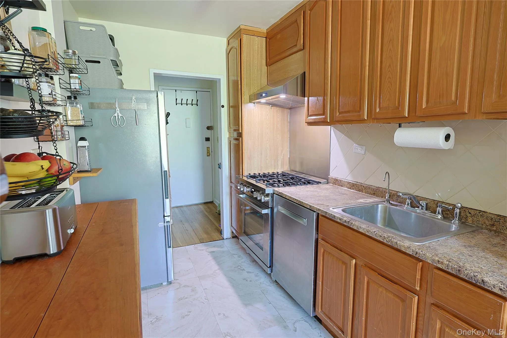 Kitchen featuring wood-finish cabinetry, stainless steel appliances, speckled stone-look countertops, and a tile backsplash Kitchen featuring wood-finish cabinetry, stainless steel appliances, speckled stone-look countertops, and a tile backsplash