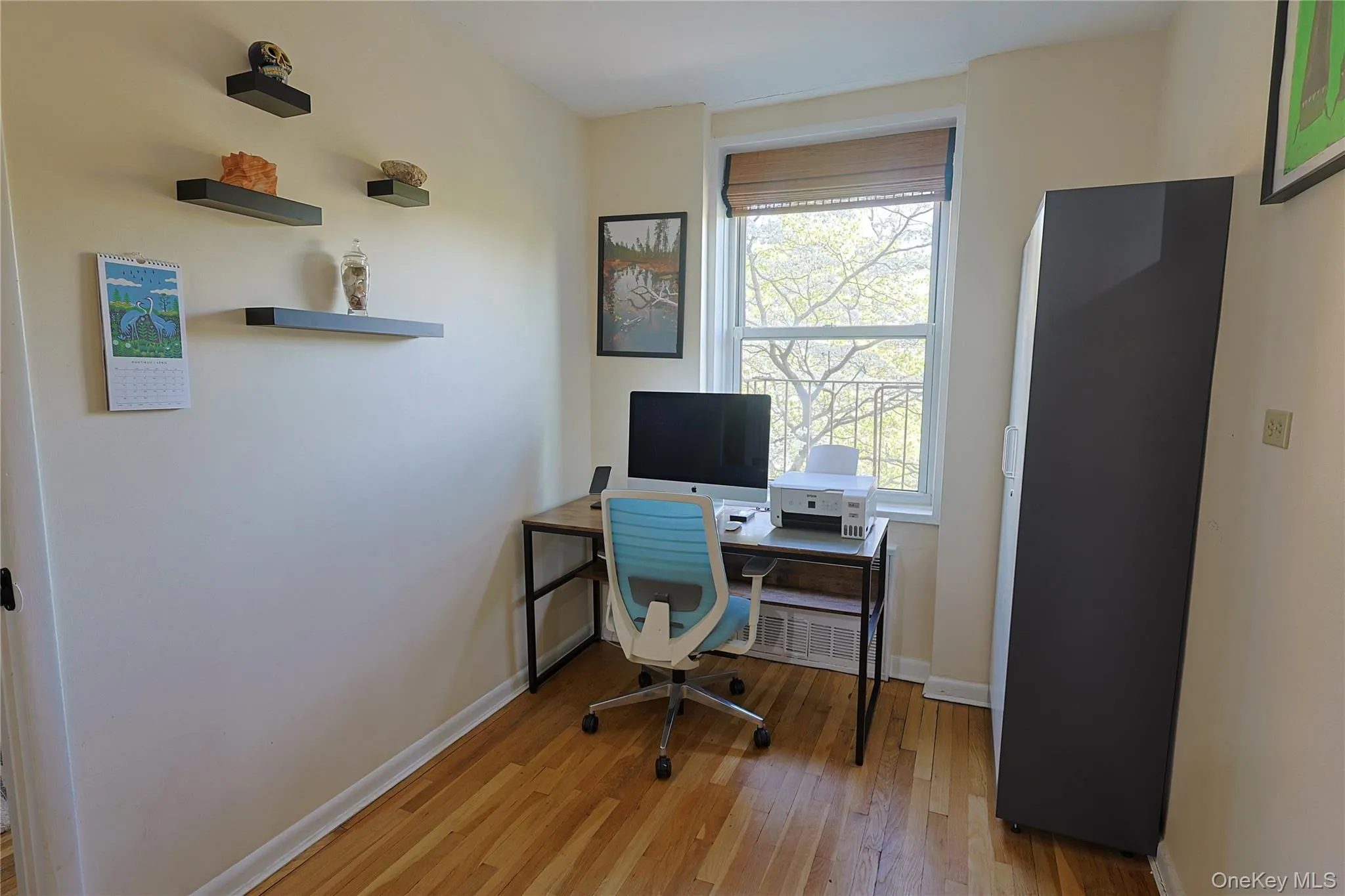 Hardwood flooring throughout this bright room, featuring a single window with slatted blinds, light-toned walls, and white baseboard trim Hardwood flooring throughout this bright room, featuring a single window with slatted blinds, light-toned walls, and white baseboard trim