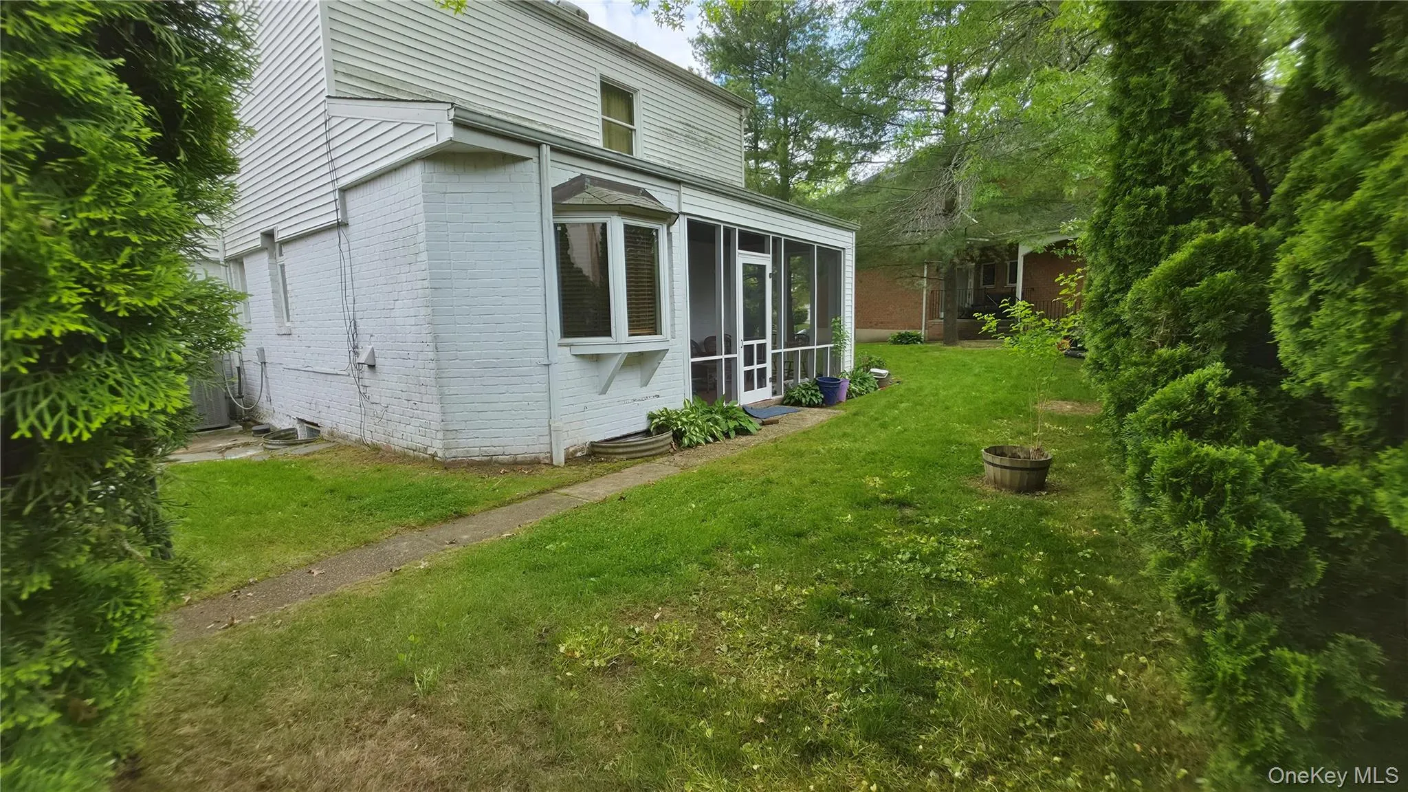 Exterior featuring a screened porch with a white frame and multiple windows, a bay window, white painted brick, white siding, and established landscaping Exterior featuring a screened porch with a white frame and multiple windows, a bay window, white painted brick, white siding, and established landscaping