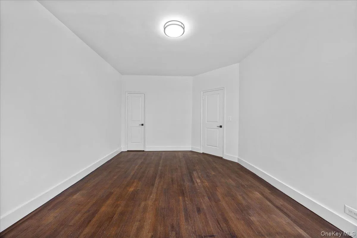 Spacious room featuring hardwood flooring, crisp white walls, white baseboards, and two paneled doors with matte black hardware Spacious room featuring hardwood flooring, crisp white walls, white baseboards, and two paneled doors with matte black hardware