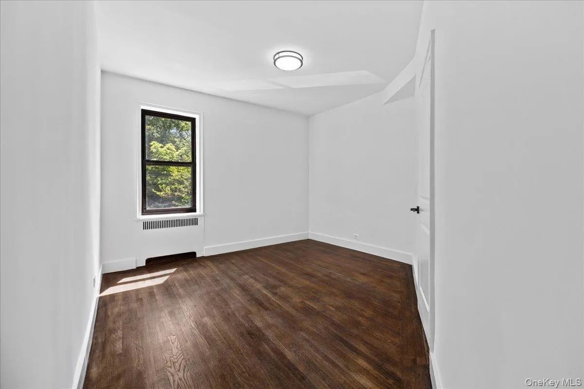 Room featuring dark wood-finish flooring, white painted walls, a flush-mount ceiling light, and a window with a dark frame Room featuring dark wood-finish flooring, white painted walls, a flush-mount ceiling light, and a window with a dark frame