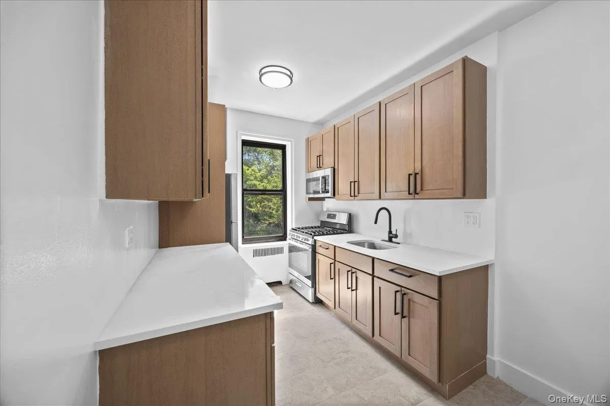 Newly renovated galley kitchen featuring light wood-finish cabinetry, light quartz countertops, and tile flooring Newly renovated galley kitchen featuring light wood-finish cabinetry, light quartz countertops, and tile flooring