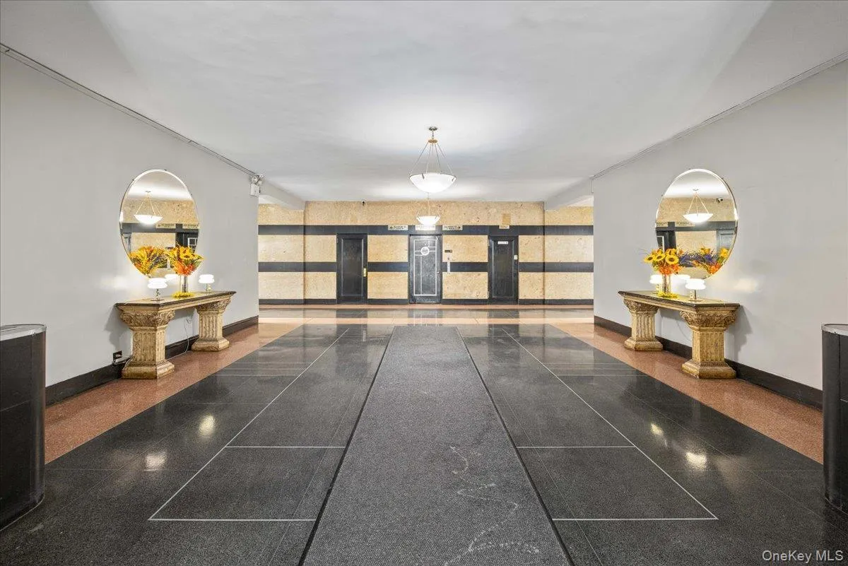 Building corridor featuring a polished stone floor, detailed console tables with oval mirrors, and a paneled wall with horizontal banding Building corridor featuring a polished stone floor, detailed console tables with oval mirrors, and a paneled wall with horizontal banding
