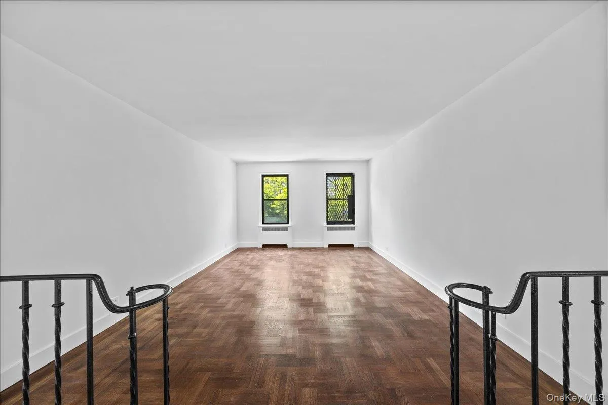 Spacious interior featuring hardwood floor, white walls, and two windows with outdoor greenery visible Spacious interior featuring hardwood floor, white walls, and two windows with outdoor greenery visible