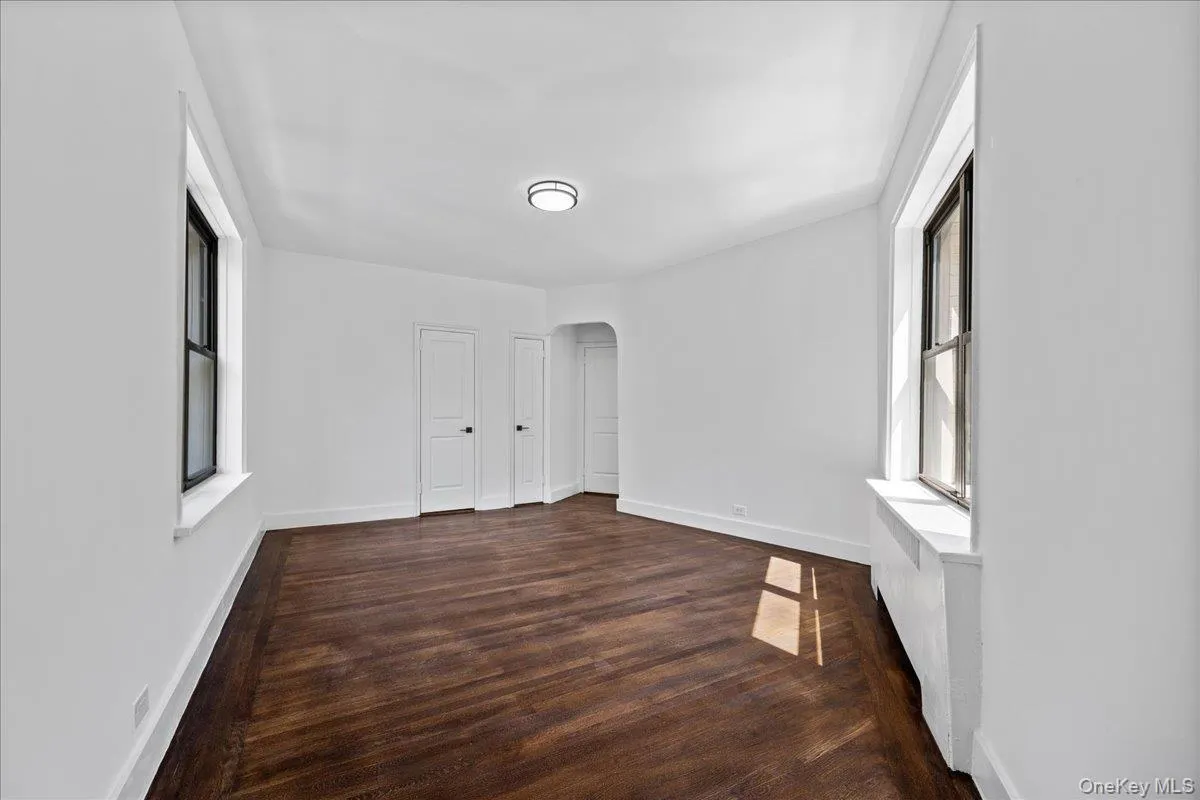 Expansive room featuring rich hardwood flooring, white baseboards, and bright white walls Expansive room featuring rich hardwood flooring, white baseboards, and bright white walls