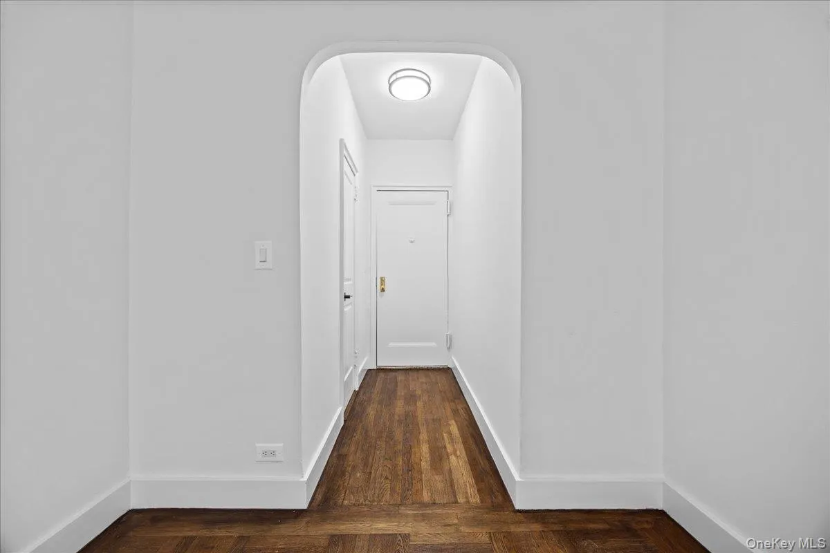 Archway entry leading to a hallway featuring wood-finish flooring, white baseboards, and a flush-mount ceiling light fixture Archway entry leading to a hallway featuring wood-finish flooring, white baseboards, and a flush-mount ceiling light fixture