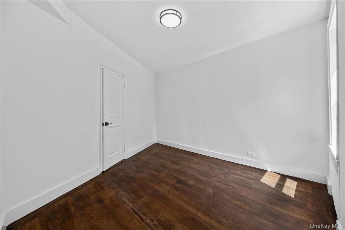 Spacious room featuring rich wood-finish flooring, crisp white walls, and a contemporary flush-mount ceiling light Spacious room featuring rich wood-finish flooring, crisp white walls, and a contemporary flush-mount ceiling light