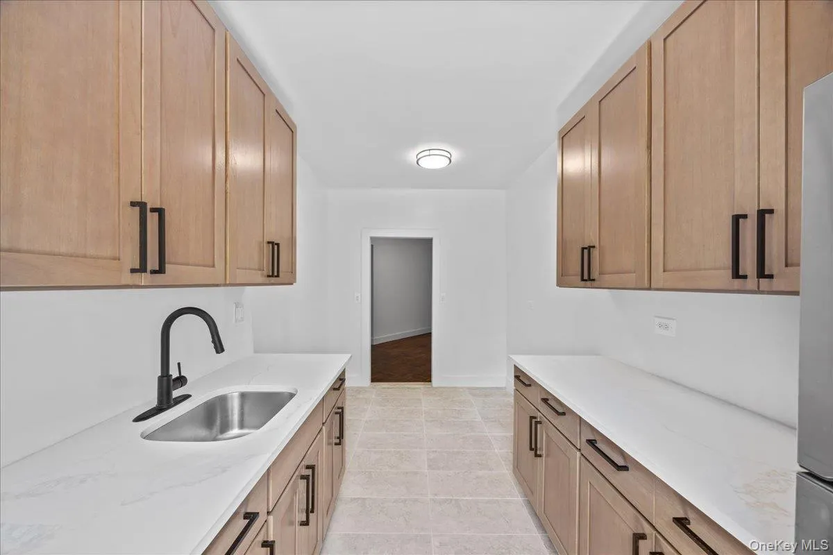 Newly renovated galley kitchen featuring light wood-finish cabinetry, light quartz countertops, and tile flooring Newly renovated galley kitchen featuring light wood-finish cabinetry, light quartz countertops, and tile flooring