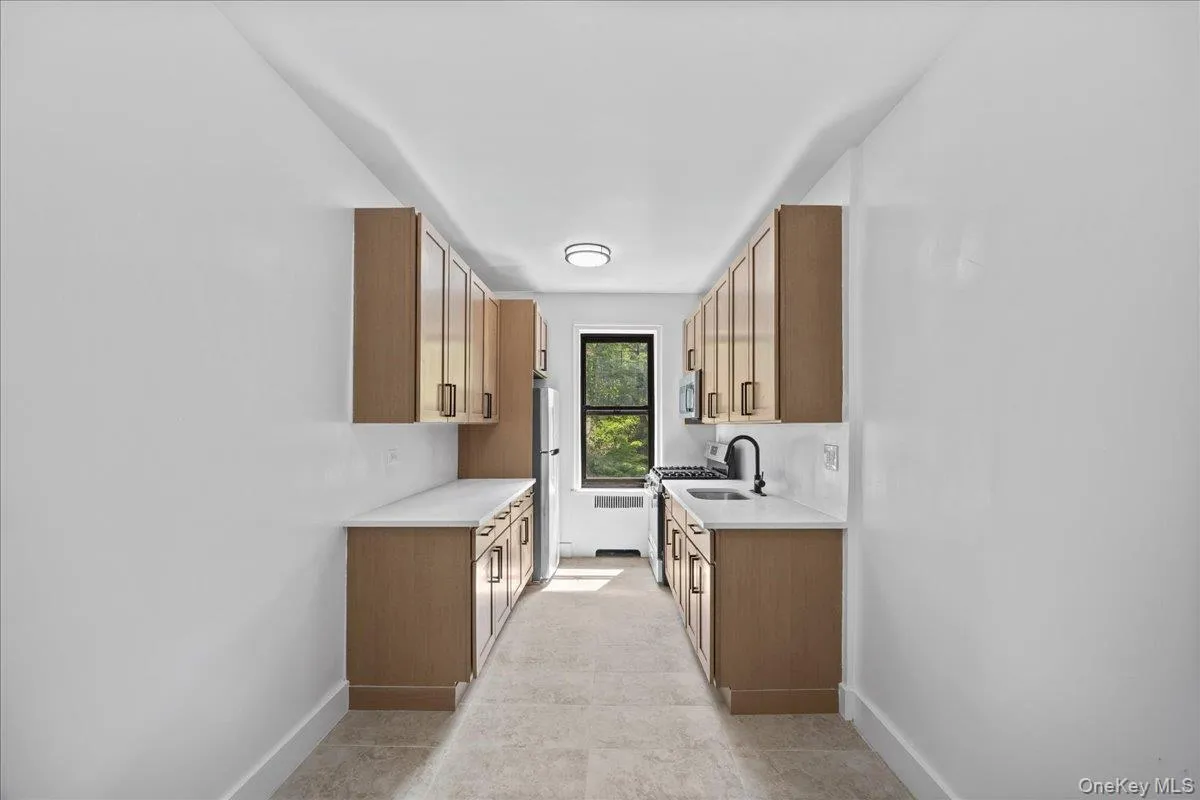 Newly renovated galley kitchen featuring light wood-finish cabinetry, light quartz countertops, and tile flooring Newly renovated galley kitchen featuring light wood-finish cabinetry, light quartz countertops, and tile flooring