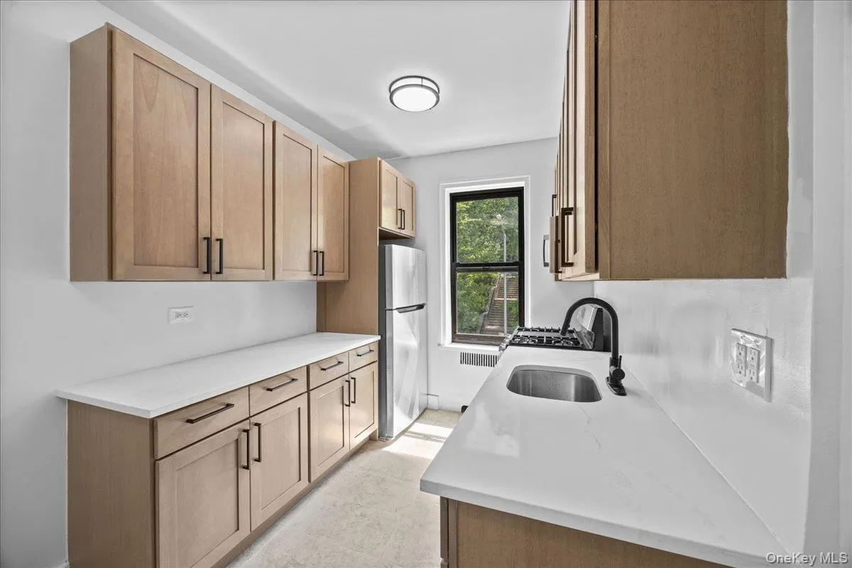 Newly renovated galley kitchen featuring light wood-finish cabinetry, light quartz countertops, and tile flooring Newly renovated galley kitchen featuring light wood-finish cabinetry, light quartz countertops, and tile flooring
