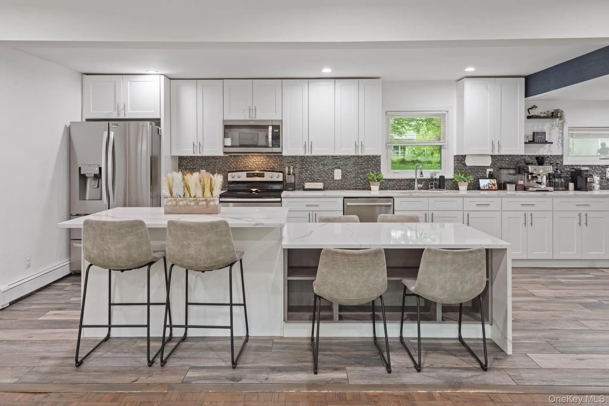 Open-concept kitchen featuring white cabinetry, stainless steel appliances, a mosaic tile backsplash, and wood-finish flooring Open-concept kitchen featuring white cabinetry, stainless steel appliances, a mosaic tile backsplash, and wood-finish flooring
