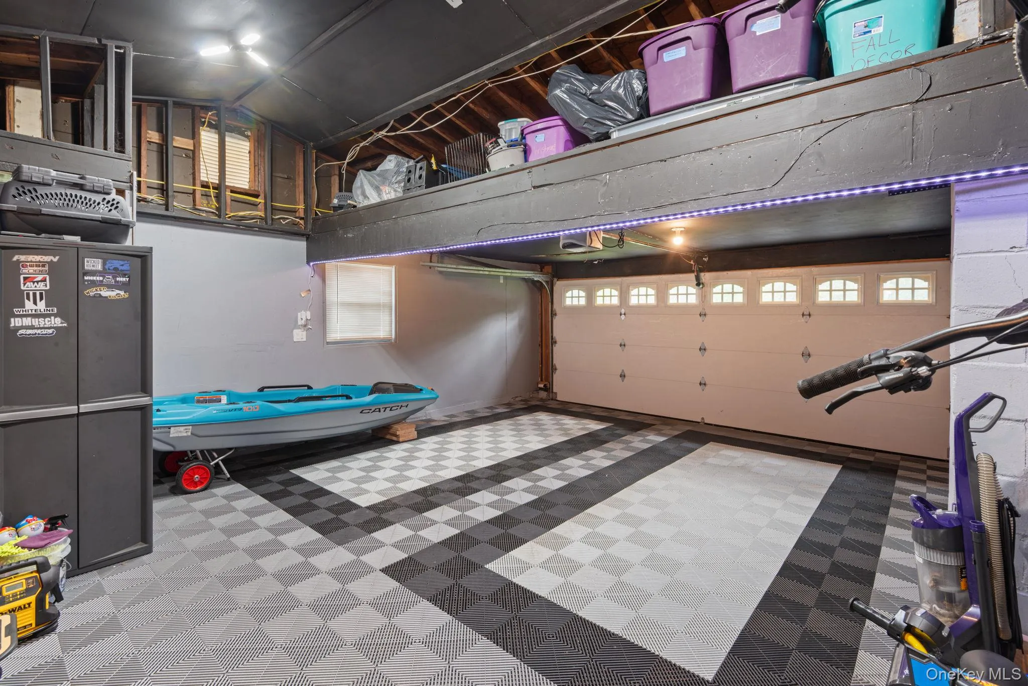 Spacious garage with overhead storage featuring checkerboard-patterned floor tiles, a windowed garage door, and recessed overhead lighting Spacious garage with overhead storage featuring checkerboard-patterned floor tiles, a windowed garage door, and recessed overhead lighting