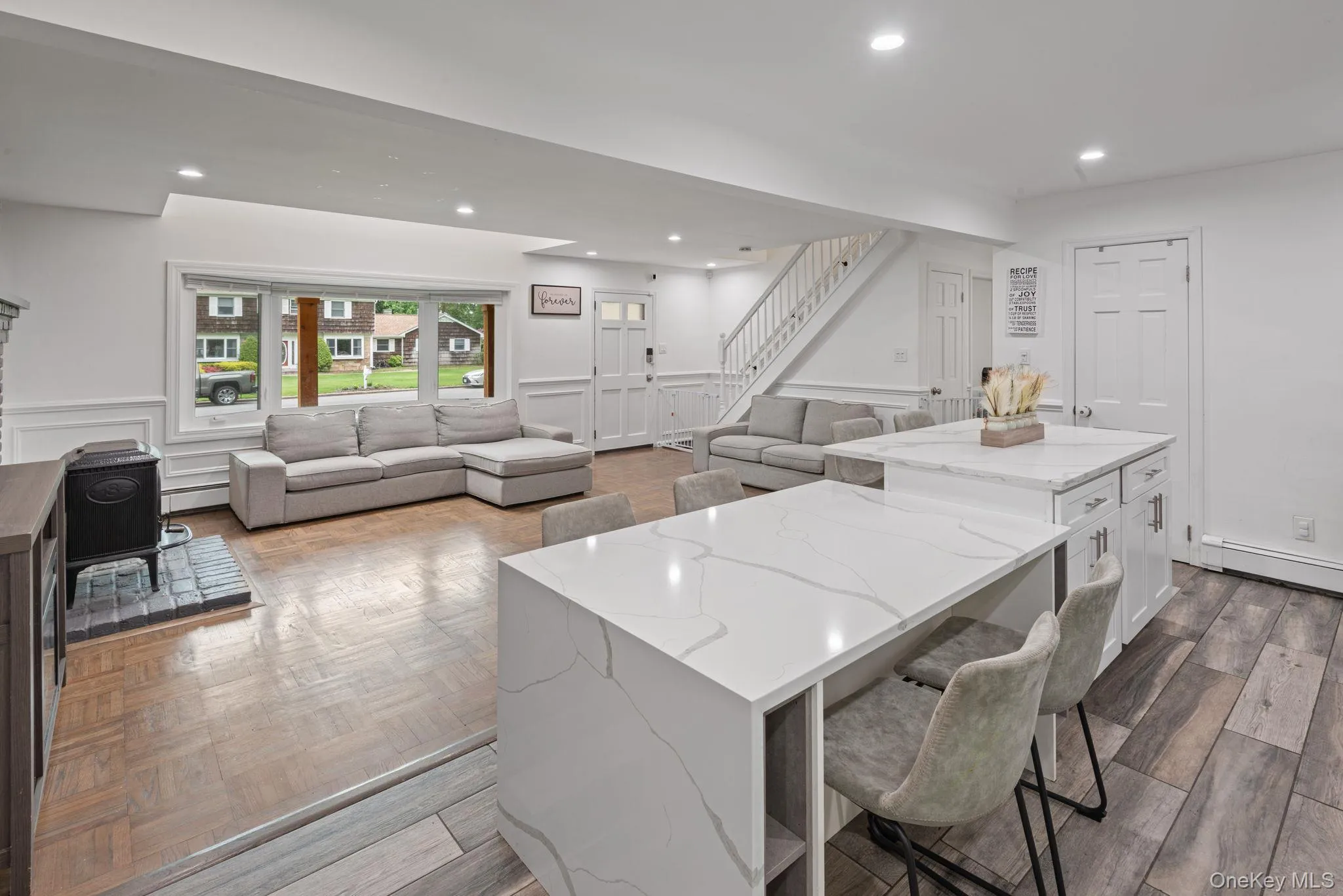 Open-concept kitchen featuring white cabinetry, stainless steel appliances, a mosaic tile backsplash, and wood-finish flooring with view into living room Open-concept kitchen featuring white cabinetry, stainless steel appliances, a mosaic tile backsplash, and wood-finish flooring with view into living room