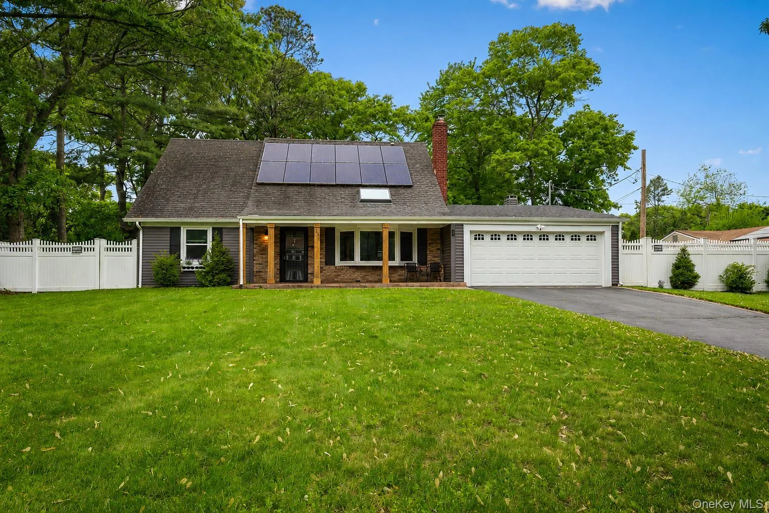 Cape Cod style single family residence featuring gray siding, a gabled roofline, solar panels, an attached two-car garage, and a white pvc fence Cape Cod style single family residence featuring gray siding, a gabled roofline, solar panels, an attached two-car garage, and a white pvc fence