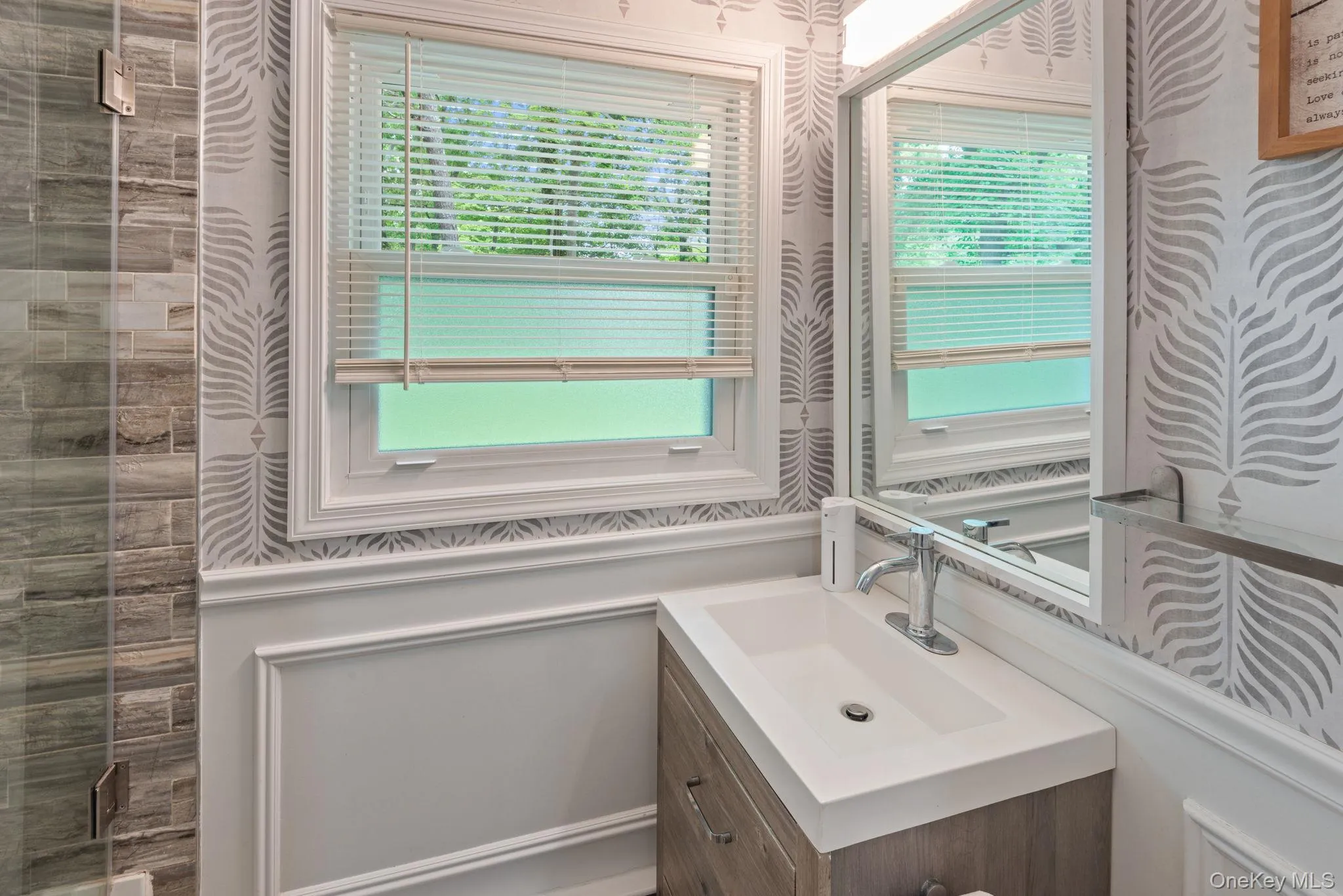 Full first floor bathroom featuring contemporary vanity with integrated sink and chrome faucet, set against patterned wallpaper and traditional wainscoting Full first floor bathroom featuring contemporary vanity with integrated sink and chrome faucet, set against patterned wallpaper and traditional wainscoting