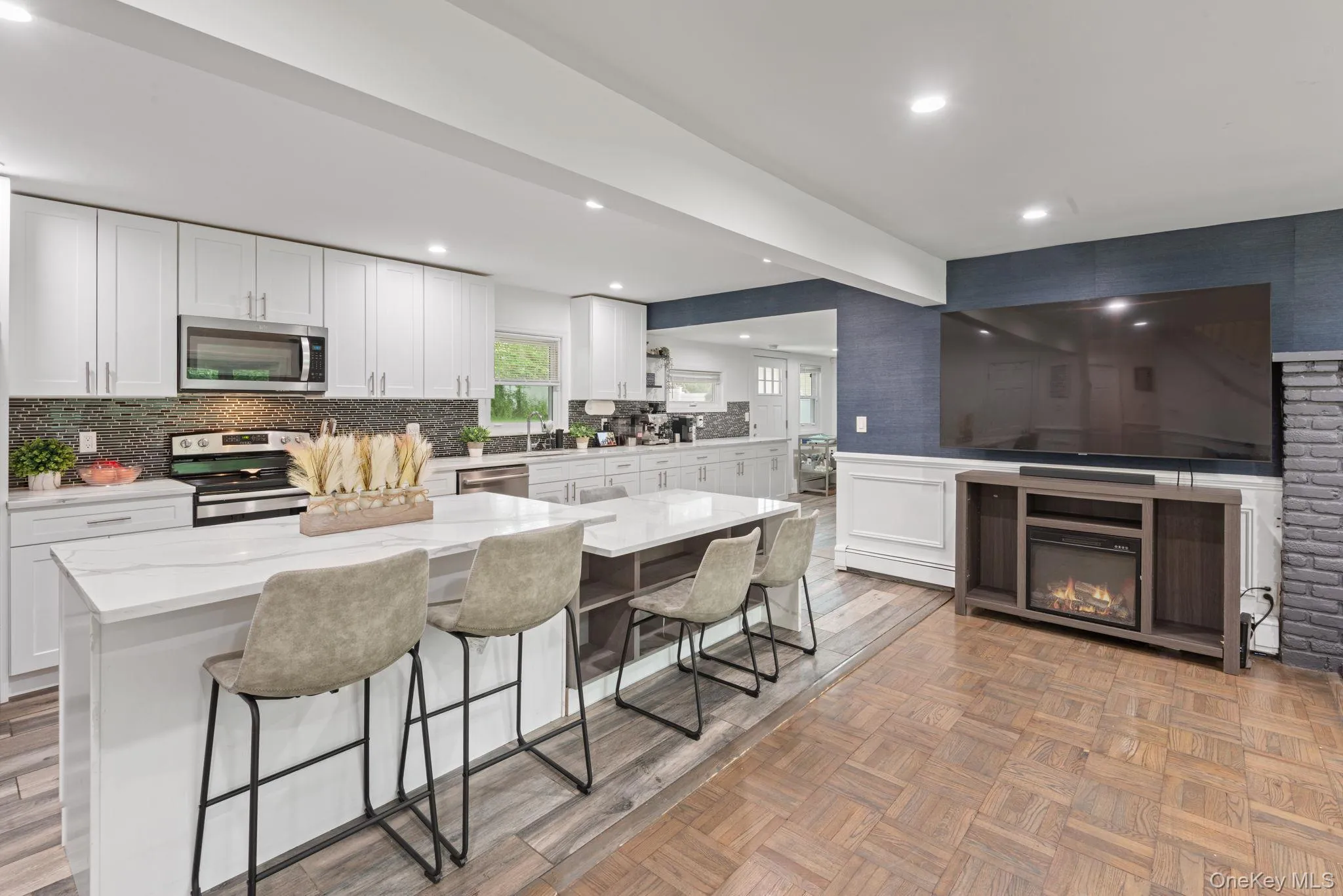 Open-concept kitchen featuring white cabinetry, stainless steel appliances, a mosaic tile backsplash, and wood-finish flooring Open-concept kitchen featuring white cabinetry, stainless steel appliances, a mosaic tile backsplash, and wood-finish flooring