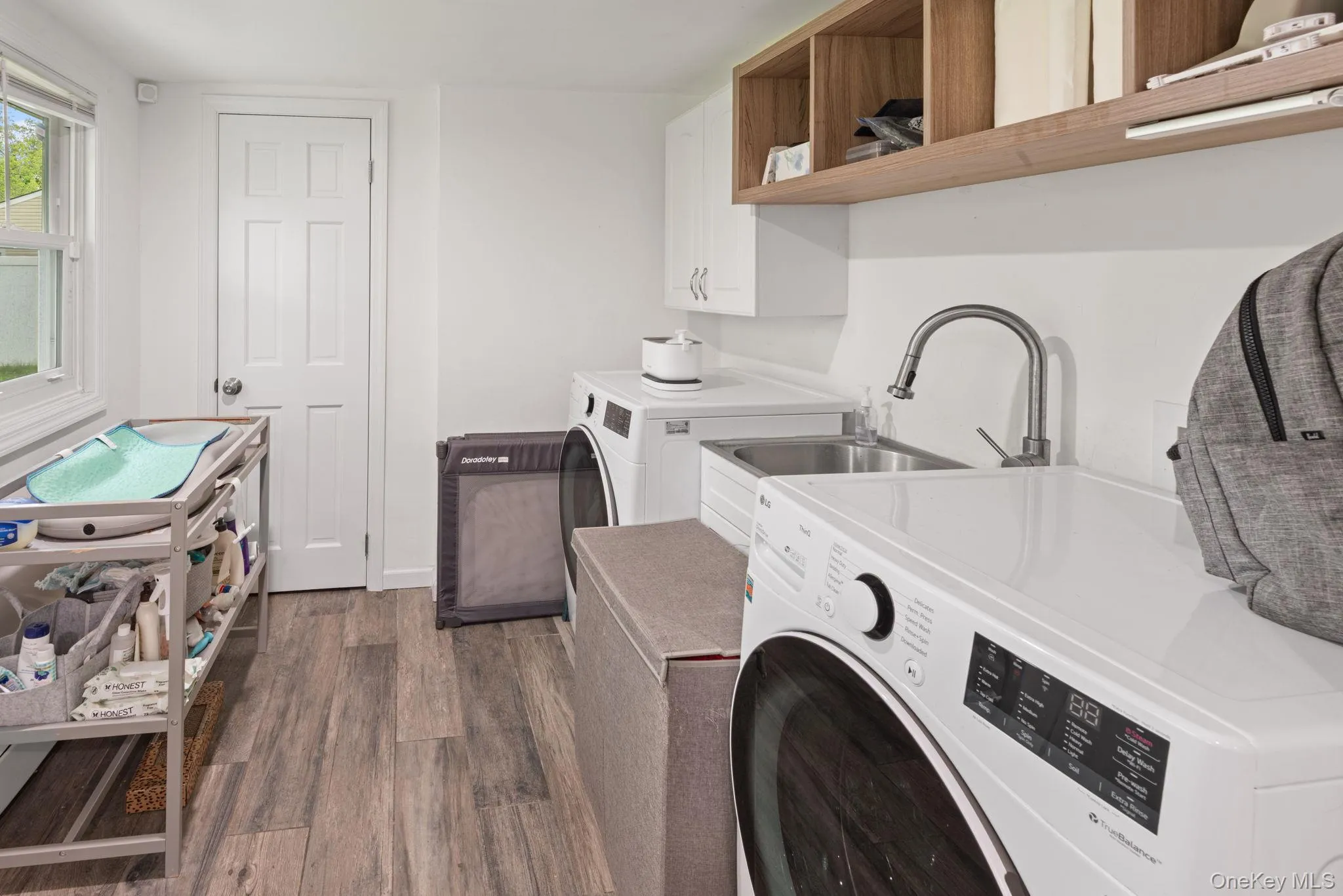 Dedicated utility space featuring wood-finish flooring, white paneled door, and a window for natural light Dedicated utility space featuring wood-finish flooring, white paneled door, and a window for natural light
