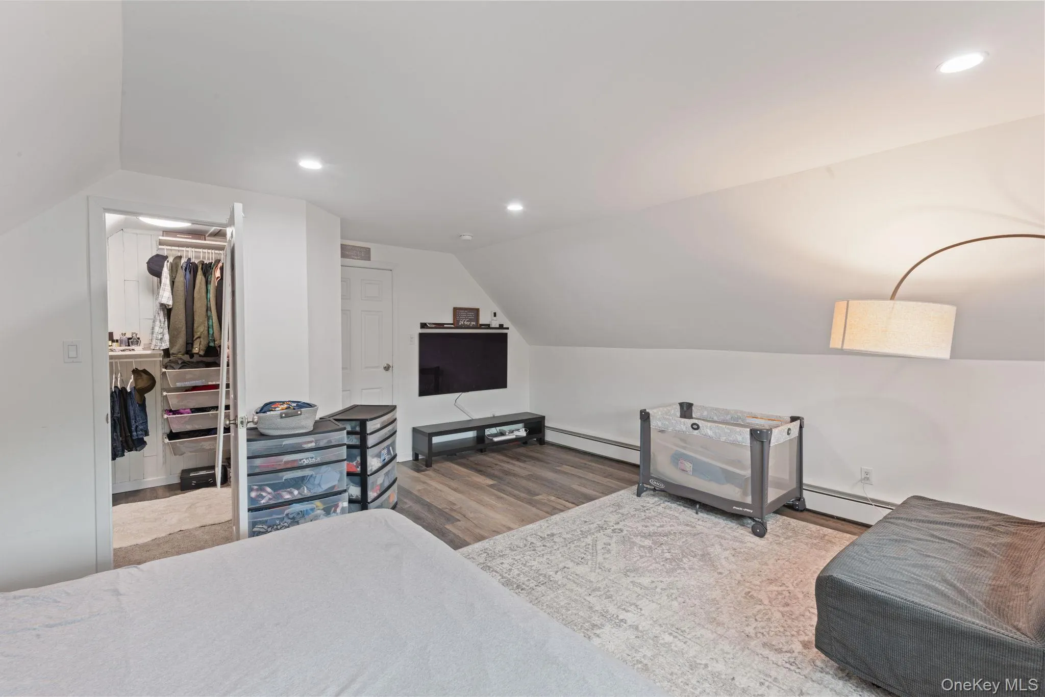 Spacious primary bedroom featuring sloped ceilings, wood-finish flooring, recessed lighting, and a walk-in closet with built-in shelving Spacious primary bedroom featuring sloped ceilings, wood-finish flooring, recessed lighting, and a walk-in closet with built-in shelving