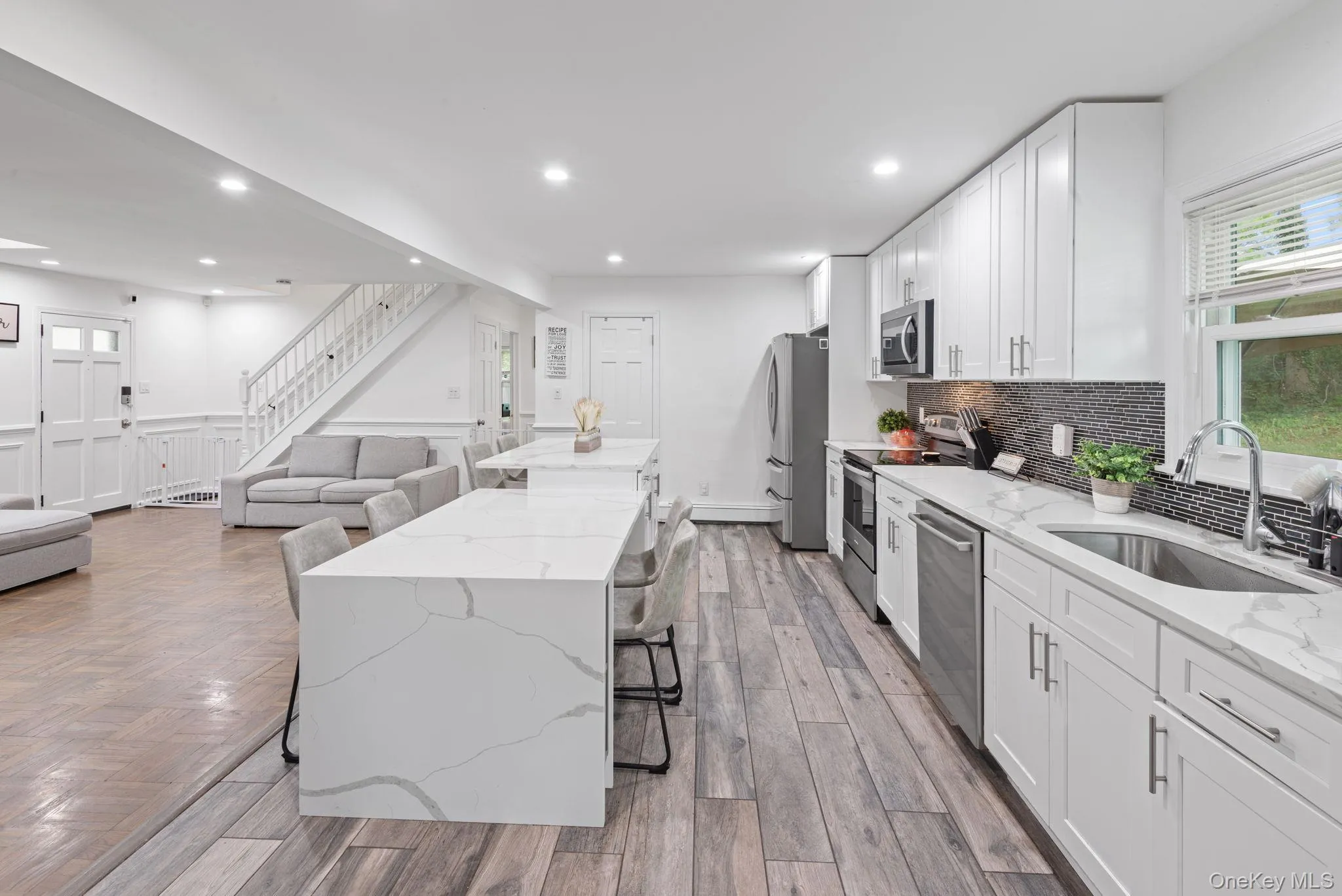 Contemporary kitchen featuring white cabinetry, integrated stainless steel appliances, and a mosaic tile backsplash Contemporary kitchen featuring white cabinetry, integrated stainless steel appliances, and a mosaic tile backsplash