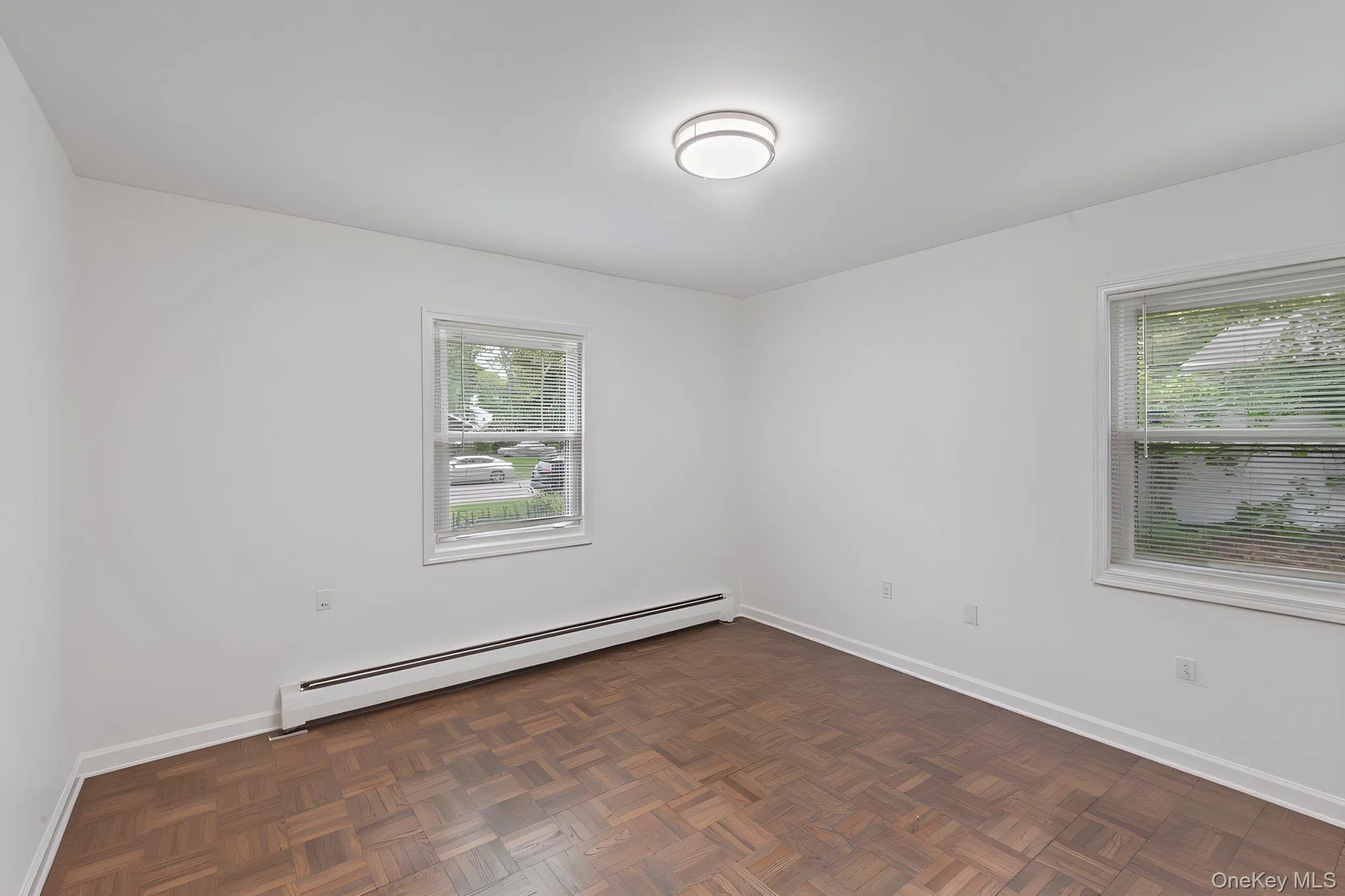 Bedroom featuring wood parquet flooring, white walls, and two windows Bedroom featuring wood parquet flooring, white walls, and two windows