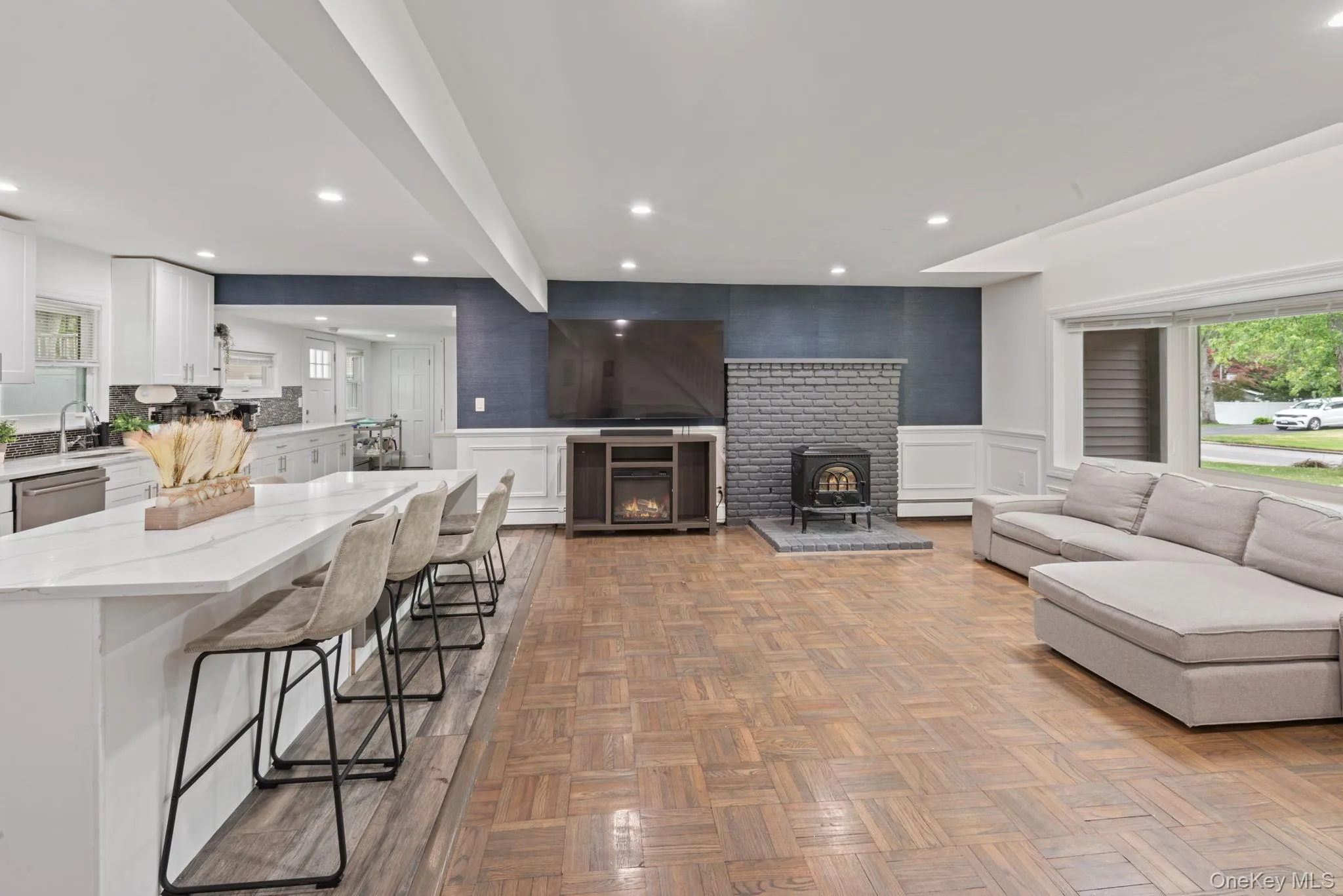 Open-concept kitchen featuring white cabinetry, stainless steel appliances, a mosaic tile backsplash, and wood-finish flooring Open-concept kitchen featuring white cabinetry, stainless steel appliances, a mosaic tile backsplash, and wood-finish flooring