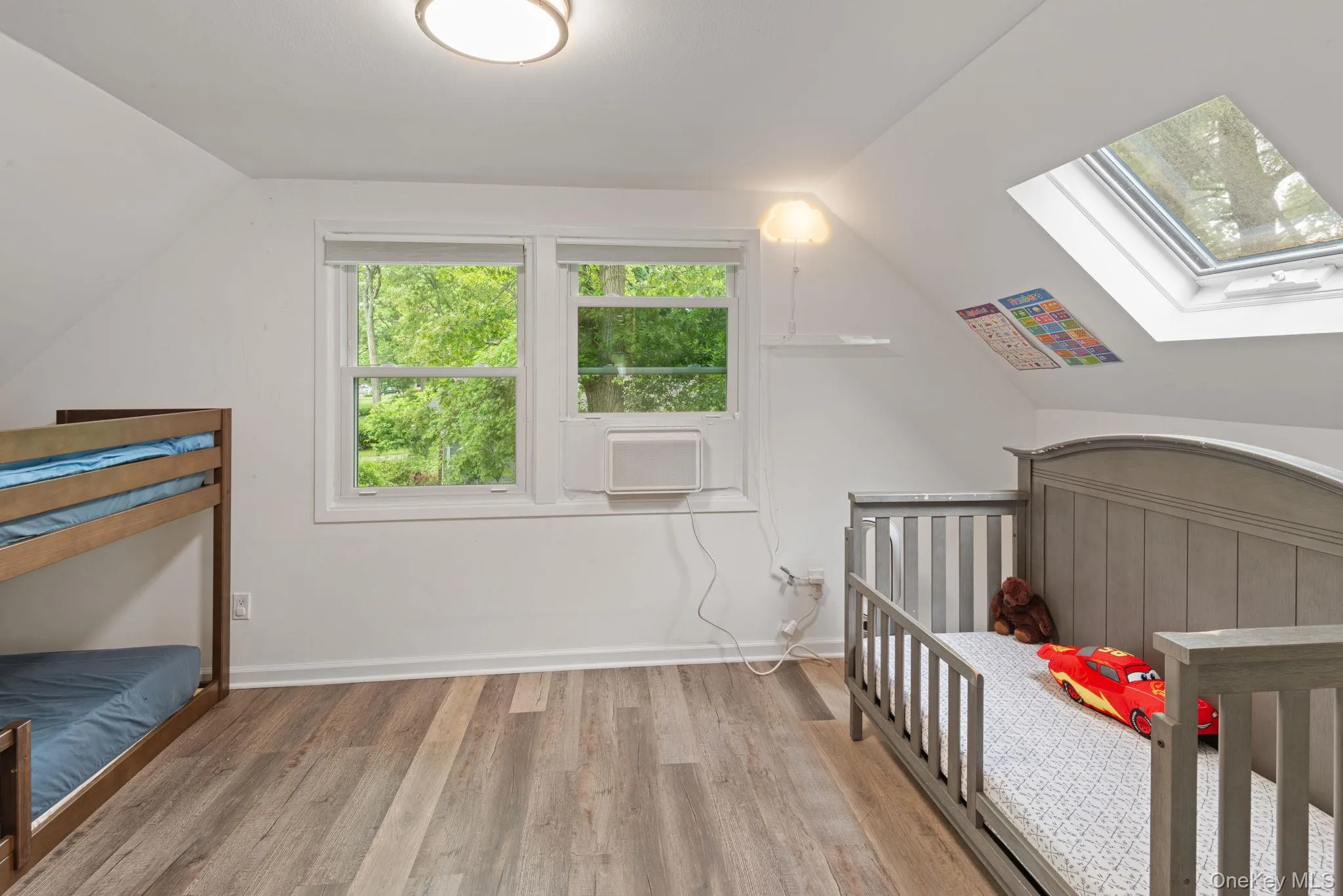 Sloped ceiling bedroom featuring wood-finish flooring with ample natural light Sloped ceiling bedroom featuring wood-finish flooring with ample natural light