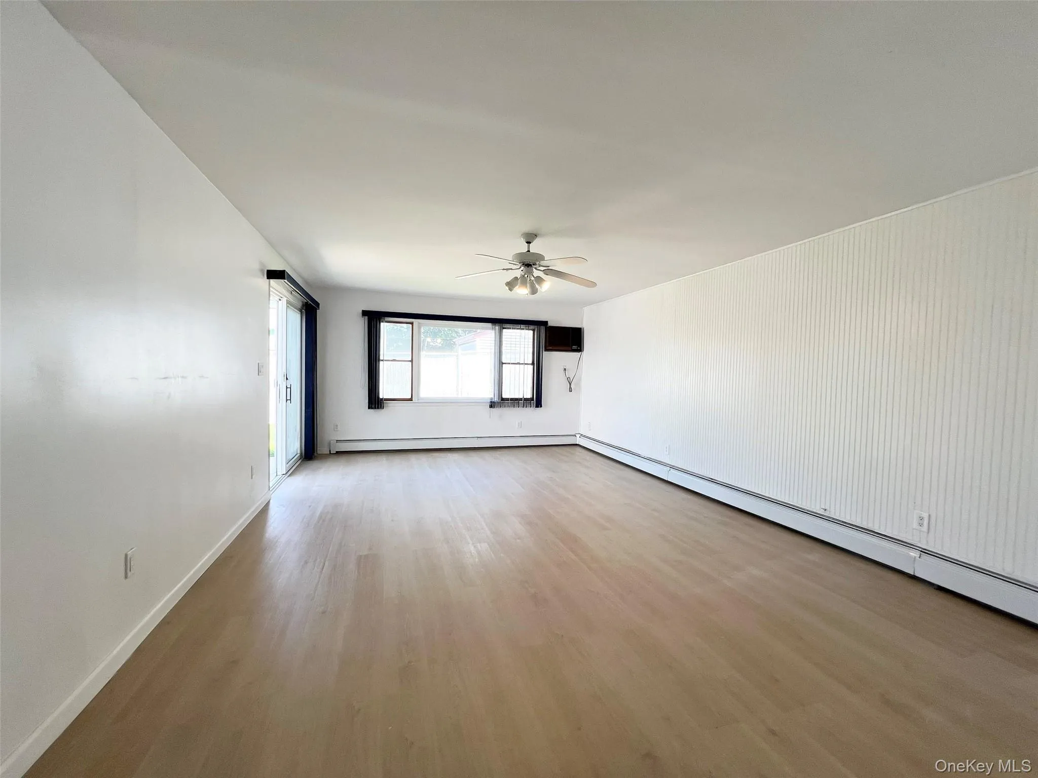 Unfurnished room featuring wood finished floors, ceiling fan, and a baseboard radiator Unfurnished room featuring wood finished floors, ceiling fan, and a baseboard radiator