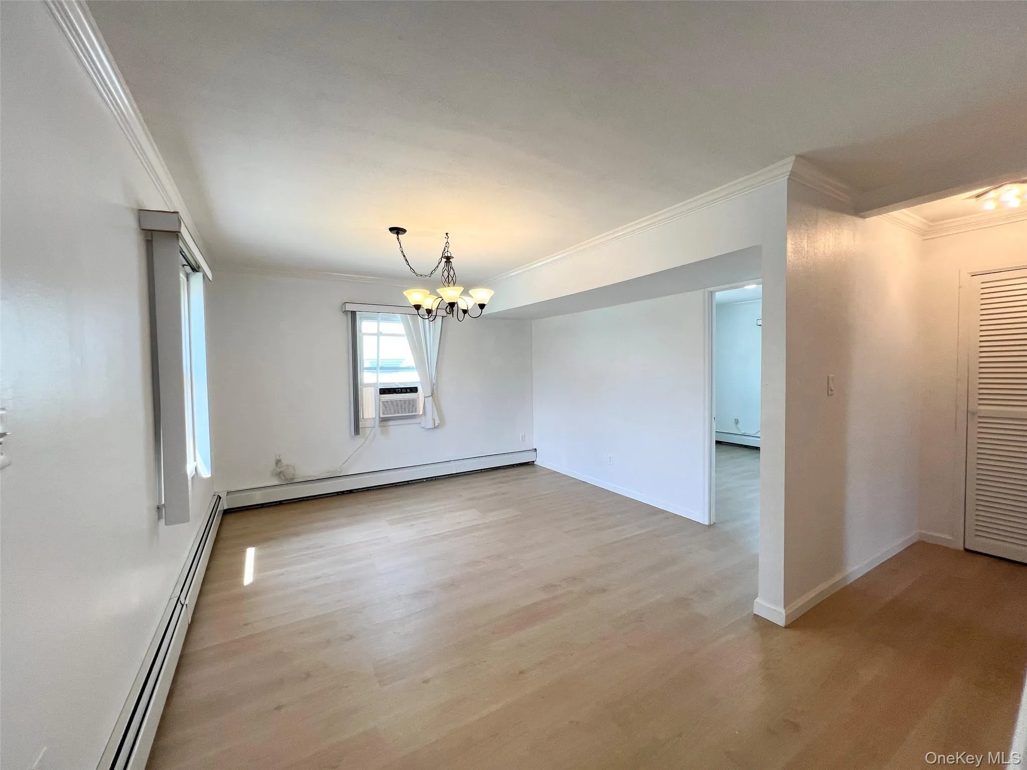 Empty room featuring crown molding, a chandelier, a baseboard radiator, and light wood-type flooring Empty room featuring crown molding, a chandelier, a baseboard radiator, and light wood-type flooring