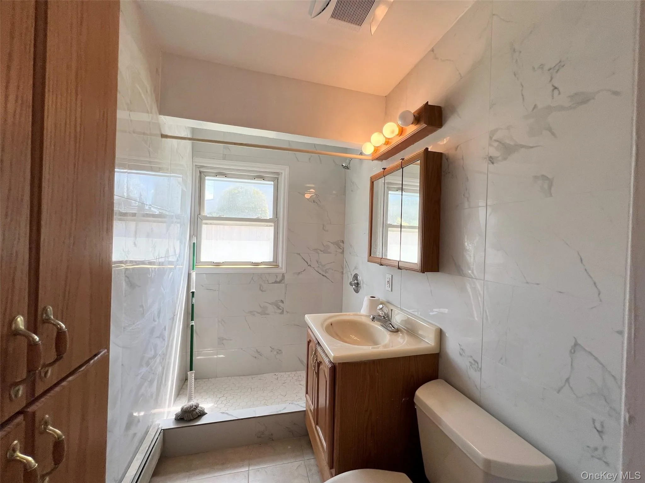 Full bath with vanity, a marble finish shower, a baseboard radiator, and healthy amount of natural light Full bath with vanity, a marble finish shower, a baseboard radiator, and healthy amount of natural light