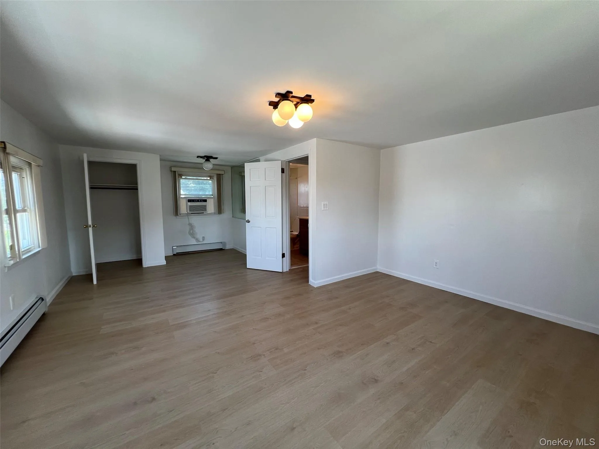 Unfurnished bedroom featuring light wood finished floors, baseboard heating, and cooling unit Unfurnished bedroom featuring light wood finished floors, baseboard heating, and cooling unit