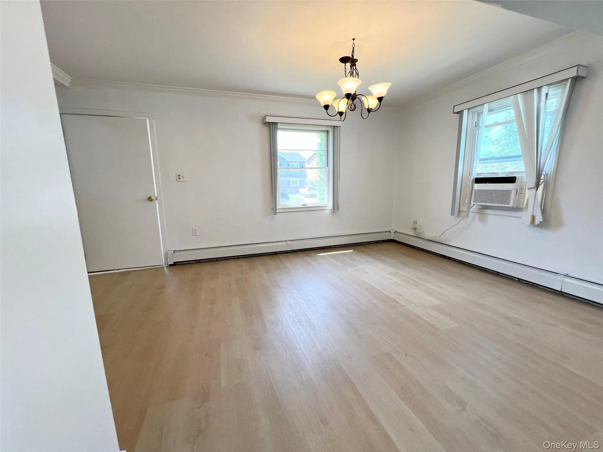 Empty room with ornamental molding, a chandelier, wood finished floors, baseboard heating, and cooling unit Empty room with ornamental molding, a chandelier, wood finished floors, baseboard heating, and cooling unit