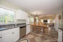 Kitchen featuring dark countertops, hanging light fixtures, stainless steel dishwasher, white cabinetry, and a sink Kitchen featuring dark countertops, hanging light fixtures, stainless steel dishwasher, white cabinetry, and a sink