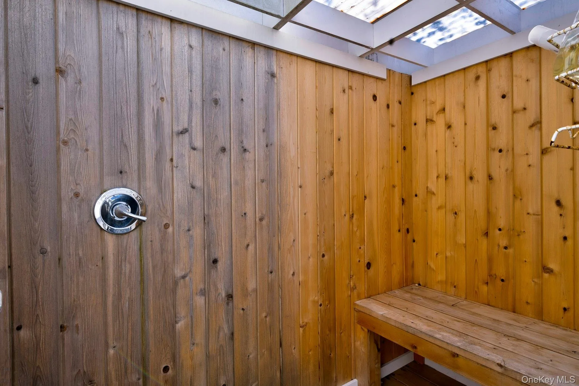 Wood-paneled outdoor shower featuring a built-in wooden bench and a chrome shower fixture Wood-paneled outdoor shower featuring a built-in wooden bench and a chrome shower fixture