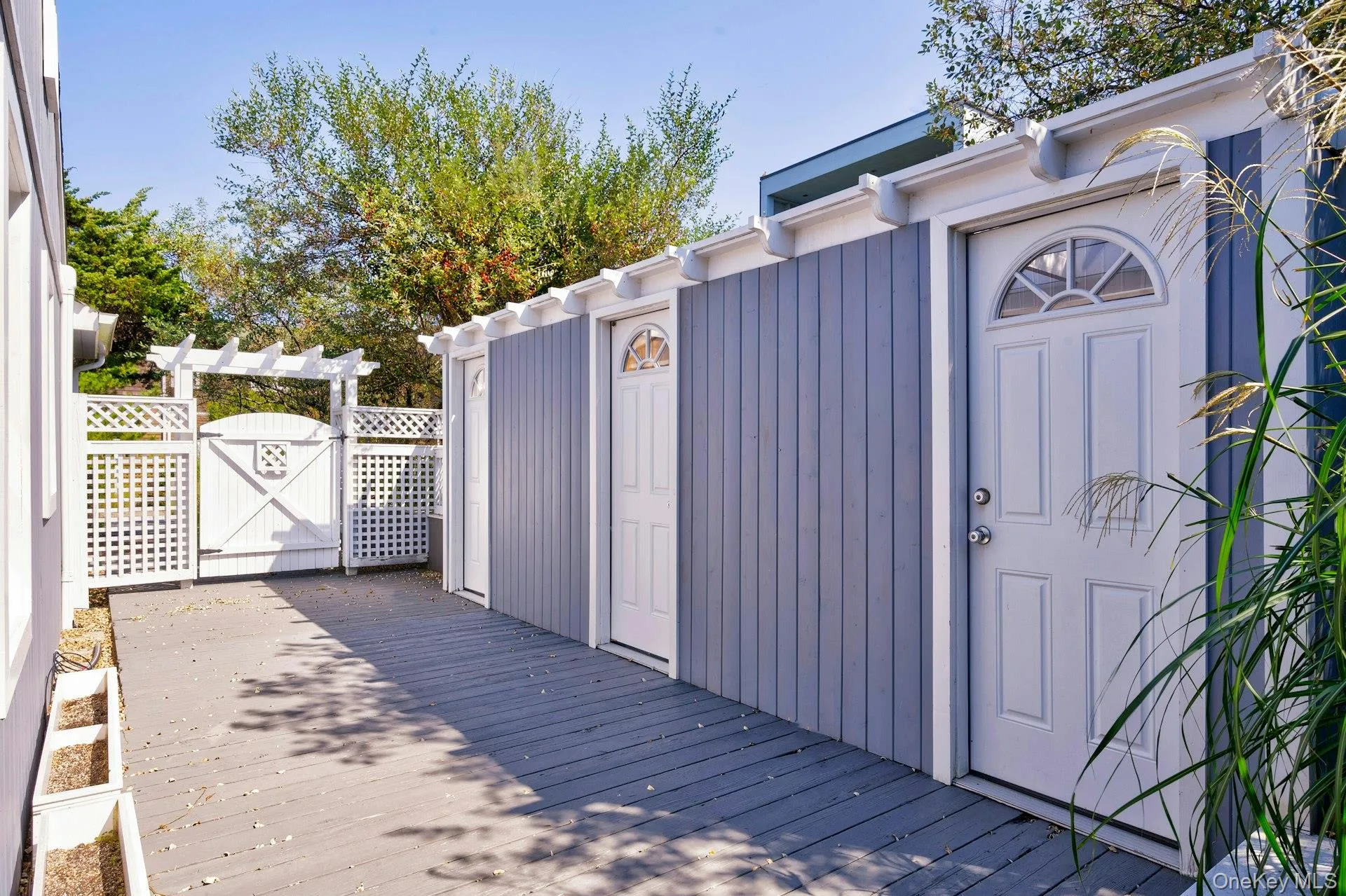 Exterior space featuring gray wood-finish decking, vertical siding in a muted blue hue, and multiple white paneled doors with arched transom windows Exterior space featuring gray wood-finish decking, vertical siding in a muted blue hue, and multiple white paneled doors with arched transom windows