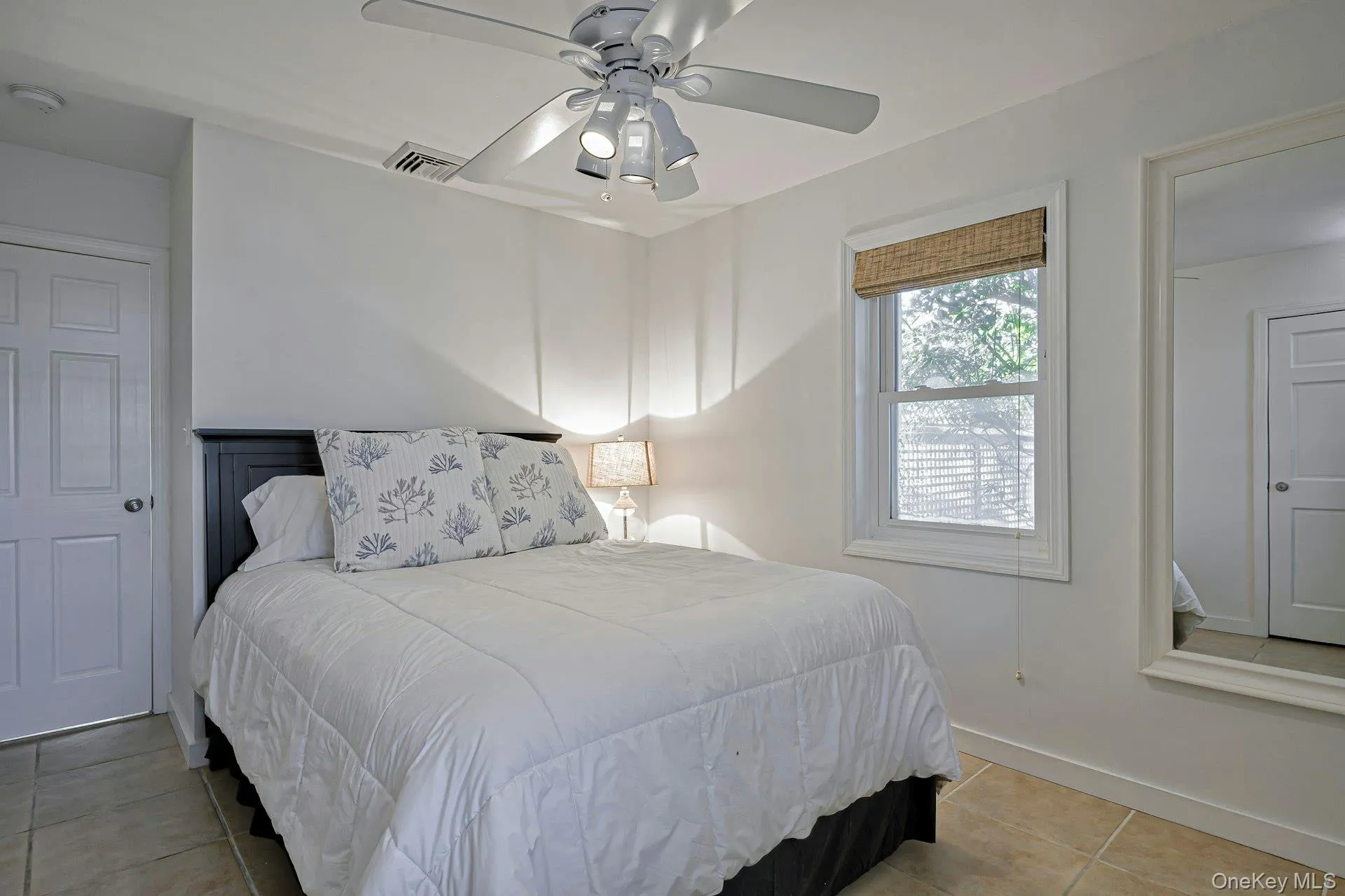 Bedroom featuring ceramic tile flooring, a window with a woven shade, a ceiling fan with integrated lighting, and white paneled doors Bedroom featuring ceramic tile flooring, a window with a woven shade, a ceiling fan with integrated lighting, and white paneled doors
