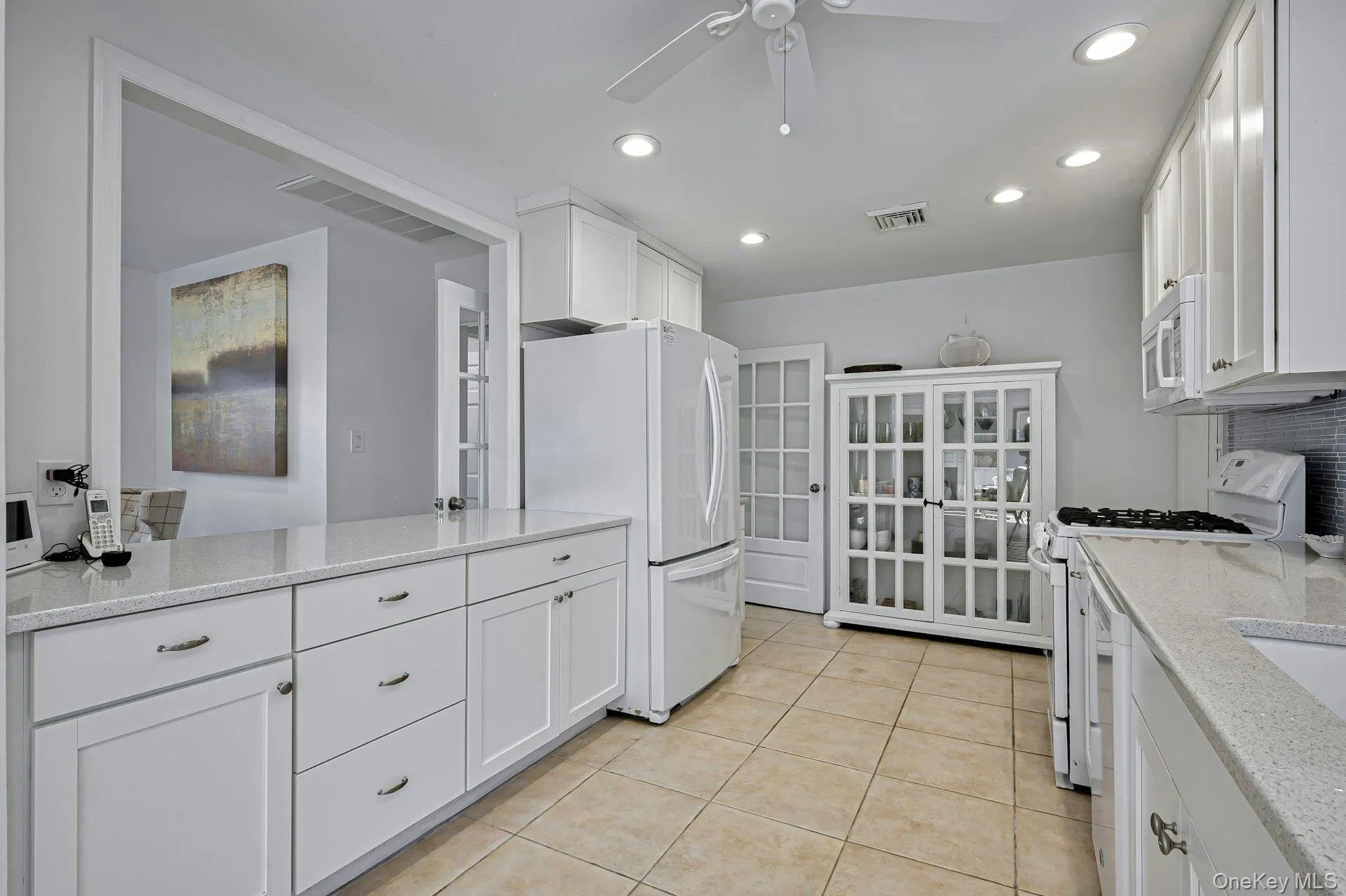 Kitchen featuring white cabinetry, light-toned countertops, recessed lighting, tile flooring, and an architectural opening Kitchen featuring white cabinetry, light-toned countertops, recessed lighting, tile flooring, and an architectural opening