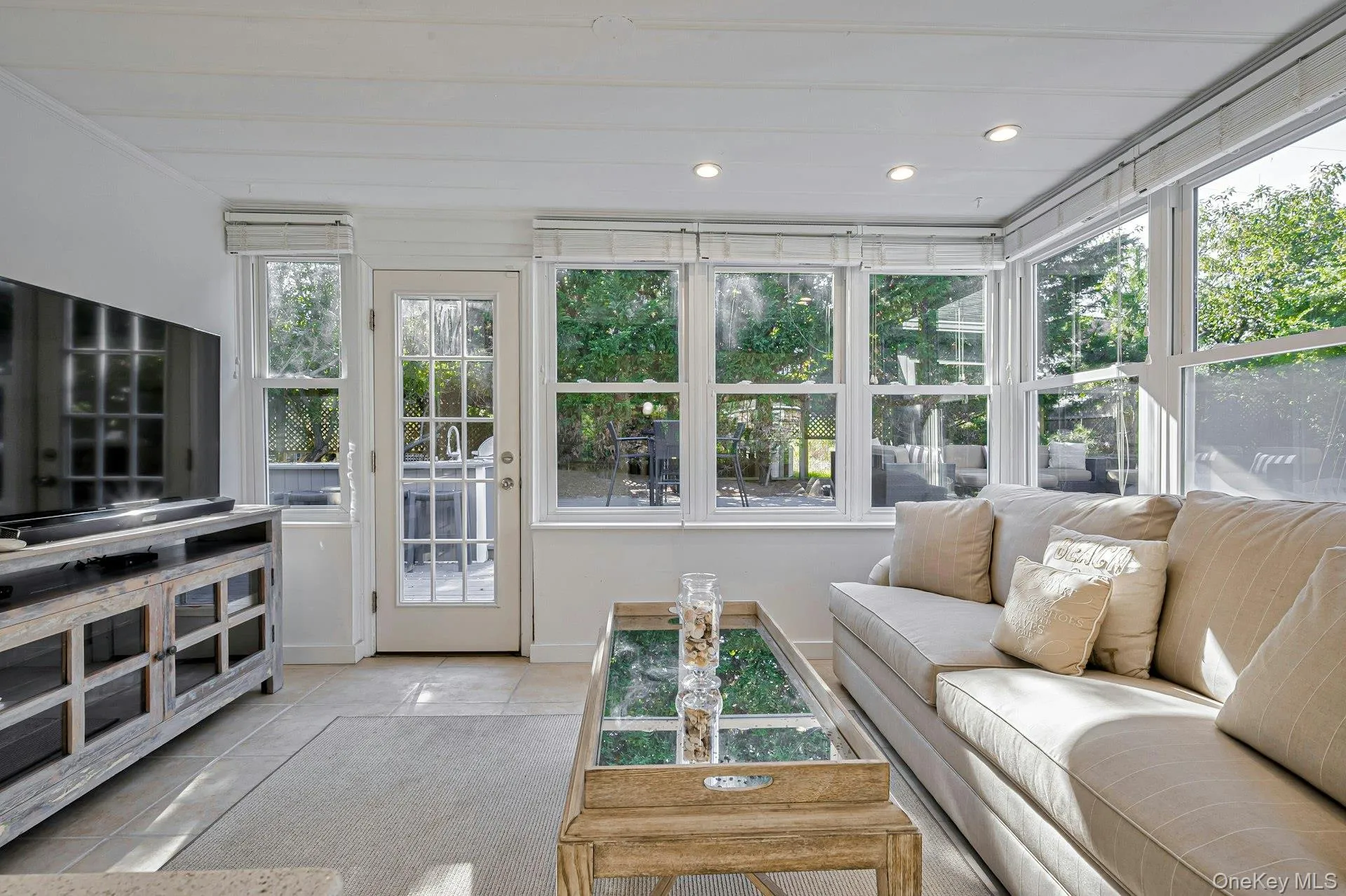 Sun-filled room featuring extensive windows, a glass-paned door, recessed lighting, white wood-plank ceiling, and light-toned tile flooring Sun-filled room featuring extensive windows, a glass-paned door, recessed lighting, white wood-plank ceiling, and light-toned tile flooring