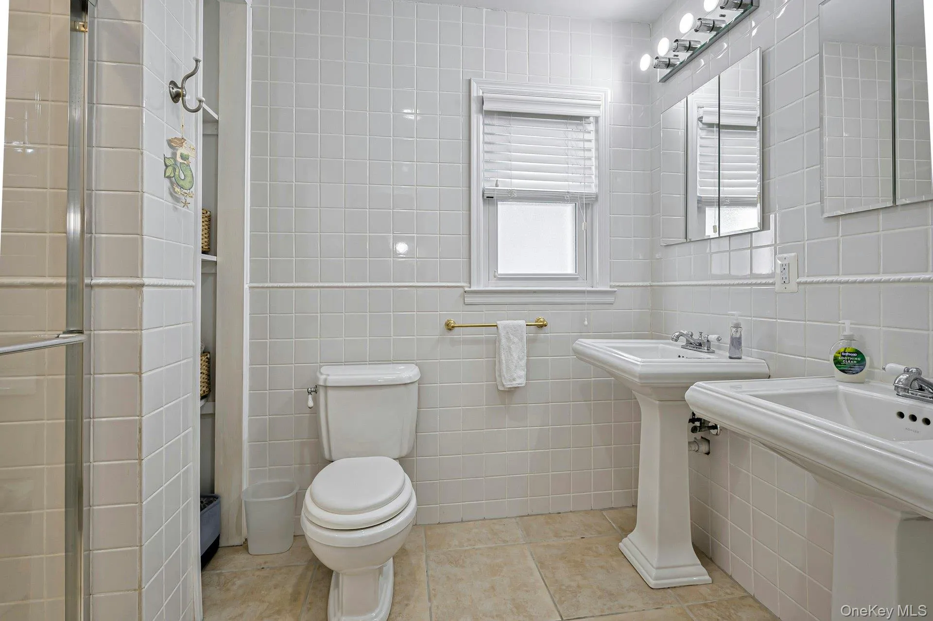 Bathroom featuring two pedestal sinks, a toilet, and a glass-enclosed shower Bathroom featuring two pedestal sinks, a toilet, and a glass-enclosed shower