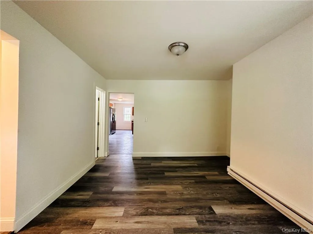 Hall with dark hardwood / wood-style floors and a baseboard heating unit Hall with dark hardwood / wood-style floors and a baseboard heating unit