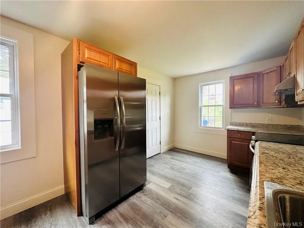 Kitchen featuring hardwood / wood-style floors, light stone countertops, and stainless steel fridge Kitchen featuring hardwood / wood-style floors, light stone countertops, and stainless steel fridge