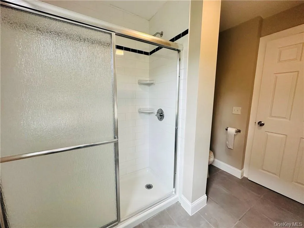 Bathroom featuring a shower with shower door, toilet, and tile floors Bathroom featuring a shower with shower door, toilet, and tile floors