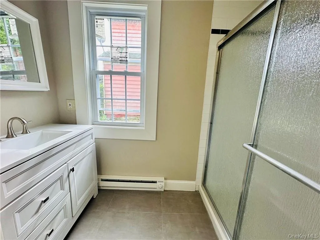 Bathroom featuring a shower with door, tile flooring, baseboard heating, and vanity Bathroom featuring a shower with door, tile flooring, baseboard heating, and vanity
