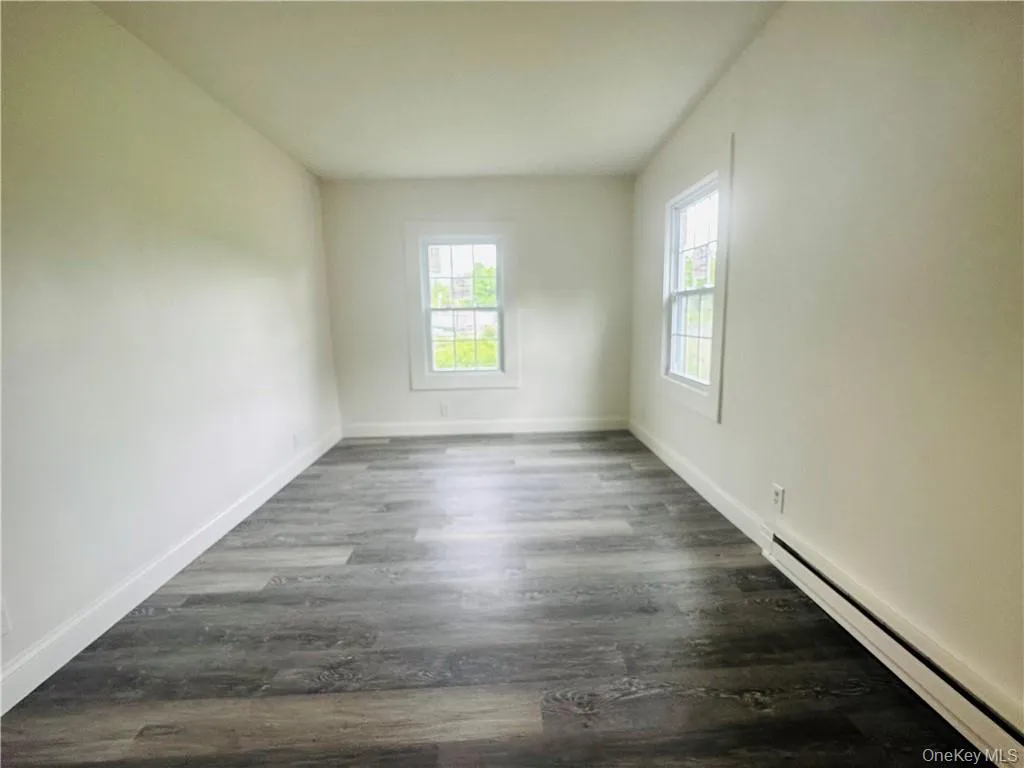 Spare room featuring a baseboard heating unit and dark hardwood / wood-style flooring Spare room featuring a baseboard heating unit and dark hardwood / wood-style flooring