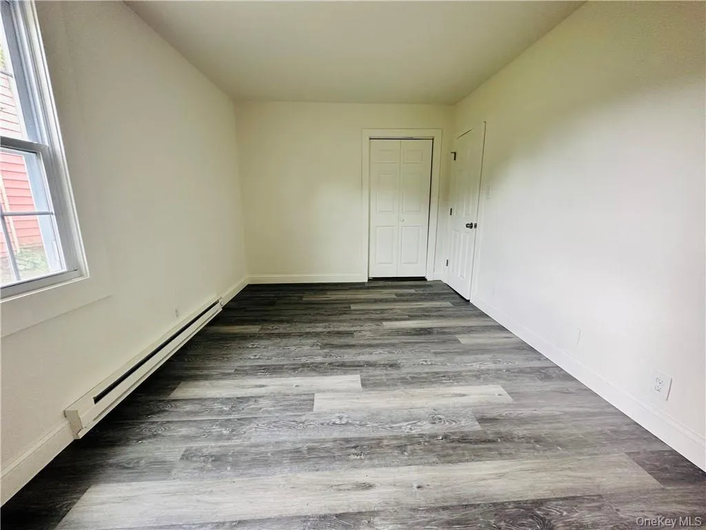 Empty room featuring a baseboard radiator and hardwood / wood-style floors Empty room featuring a baseboard radiator and hardwood / wood-style floors
