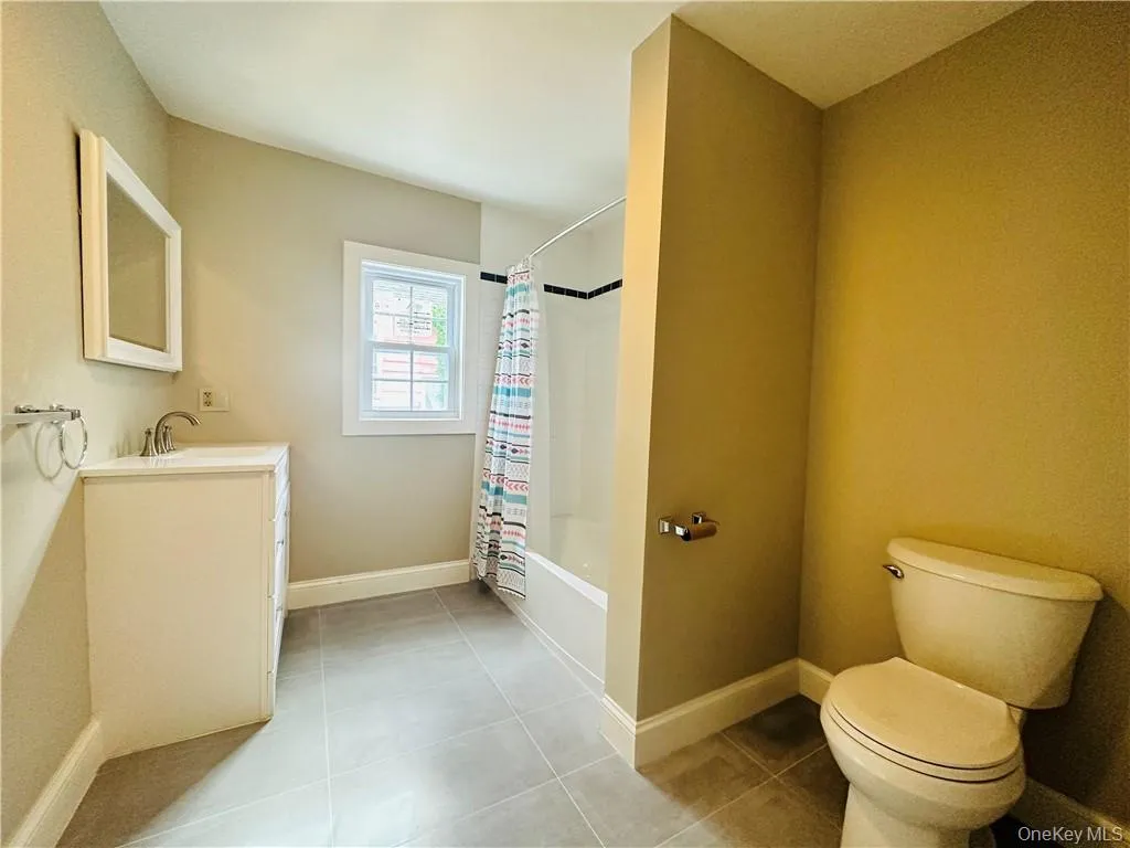 Full bathroom featuring tile floors, shower / bath combination with curtain, vanity, and toilet Full bathroom featuring tile floors, shower / bath combination with curtain, vanity, and toilet